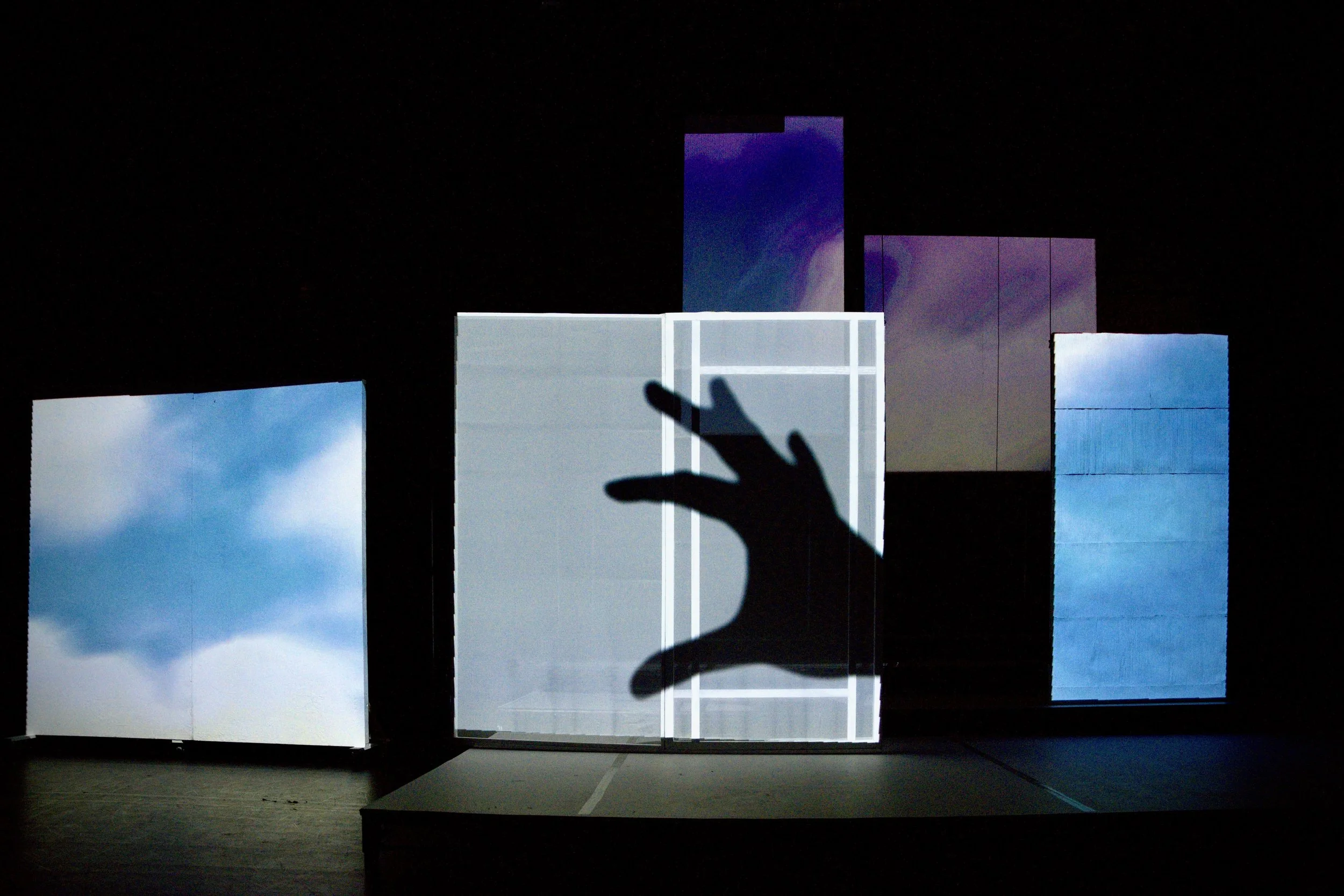 A projection of a sky filled with clouds and a rainbow on a screen, with a dark silhouette of a hand reaching towards it.