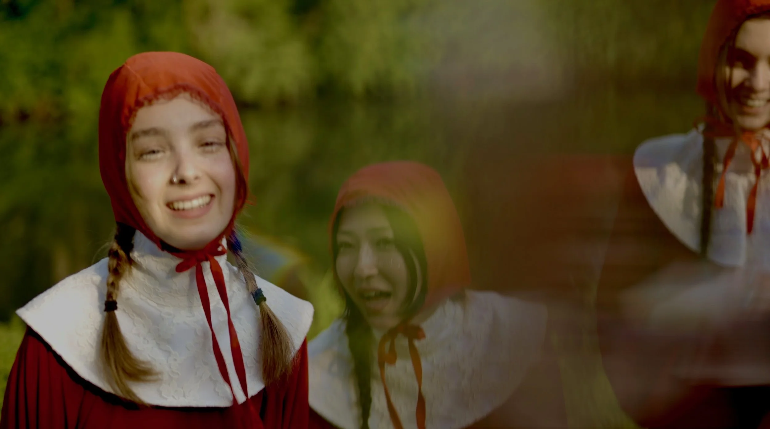 Group of young women outdoors, wearing vintage-style white blouses and red headscarves, smiling and enjoying time together.
