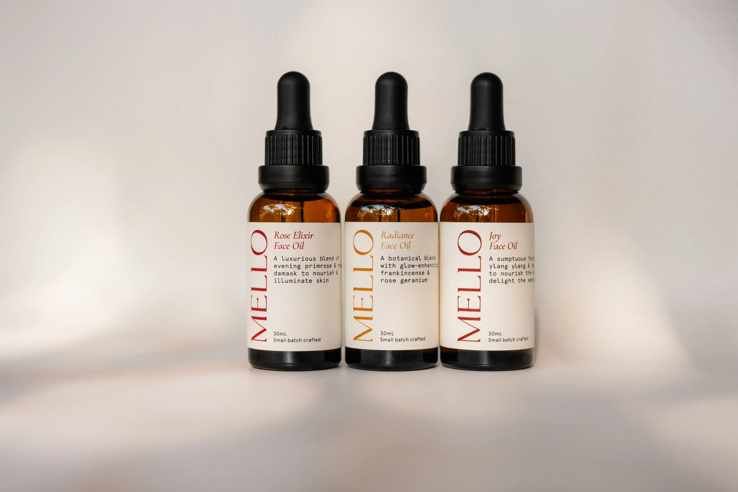 Three amber glass dropper bottles with black caps lined up on a white surface, each labeled as face oil with different scents and descriptions.