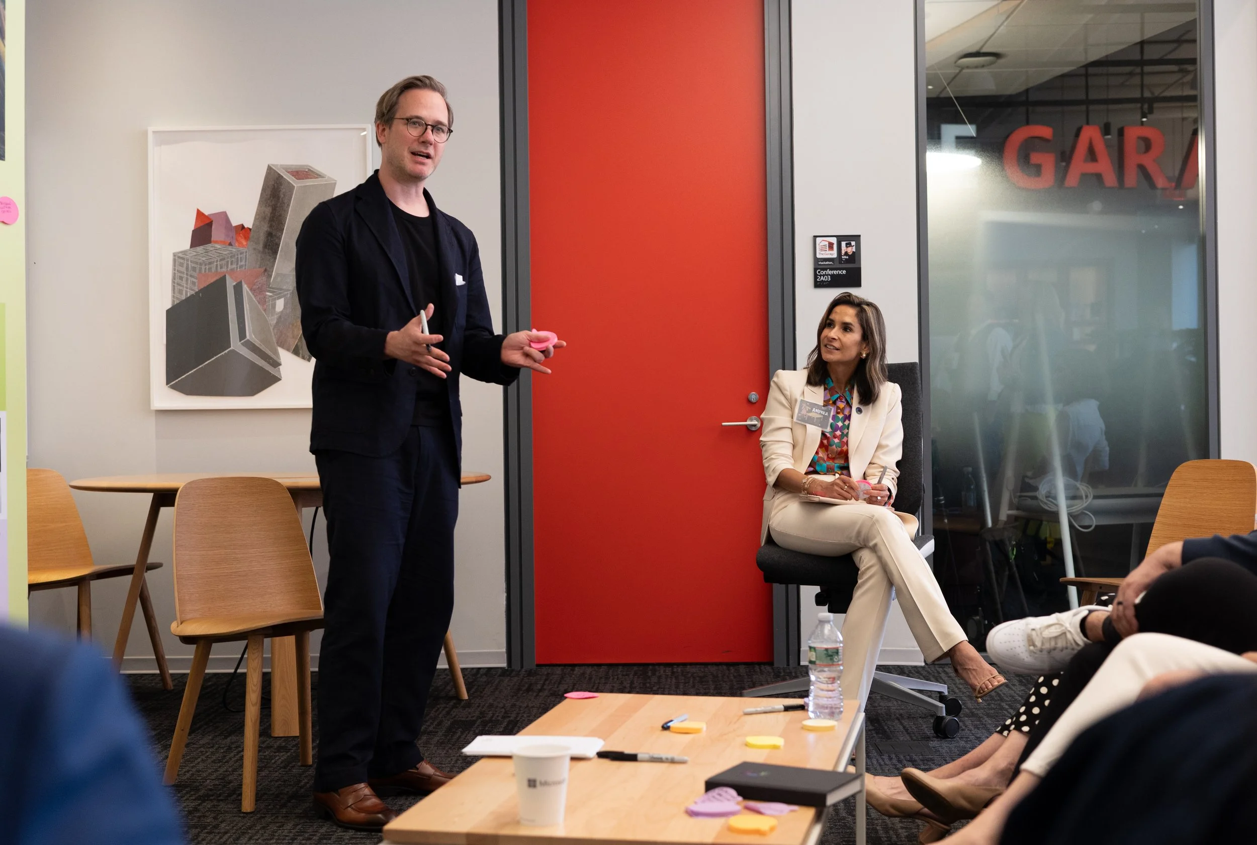 A corporate event professional photo of a man with glasses and a woman, possibly in a professional or conference setting, engaging in a discussion or presentation in an office or conference room.