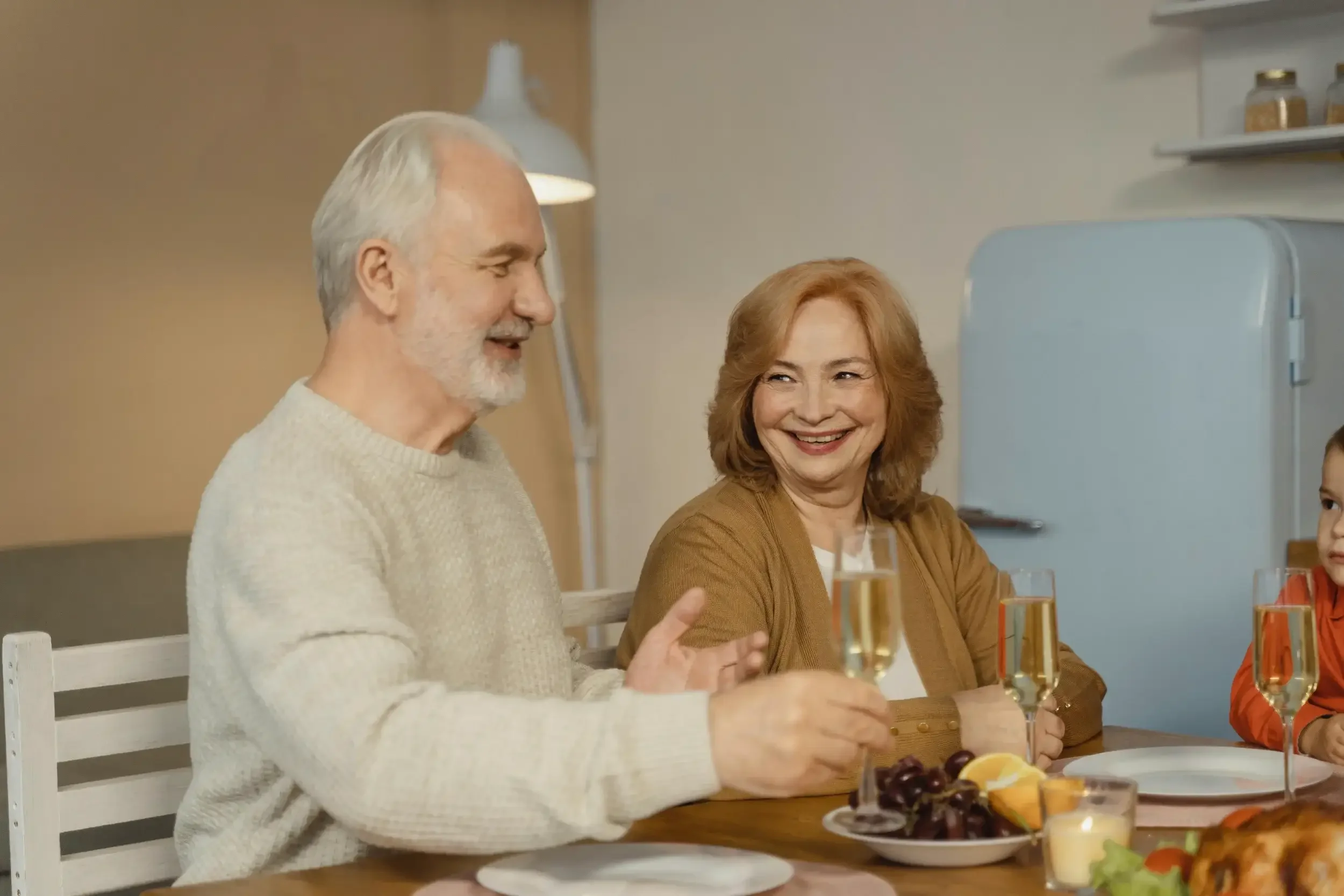 A group of people sitting around a table enjoying drinks and food, smiling and talking, in a cozy indoor setting.