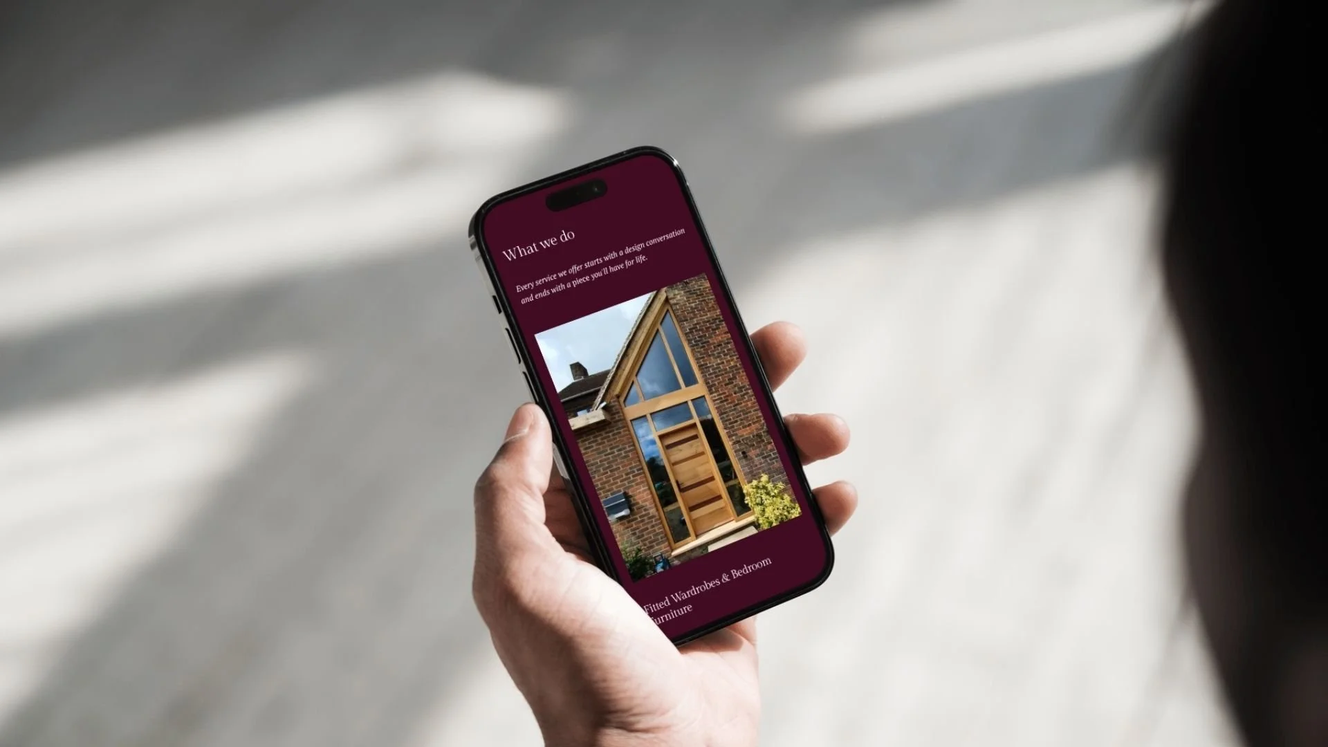 Person holding a smartphone with a website showing a brick house with wooden accents and a garden.