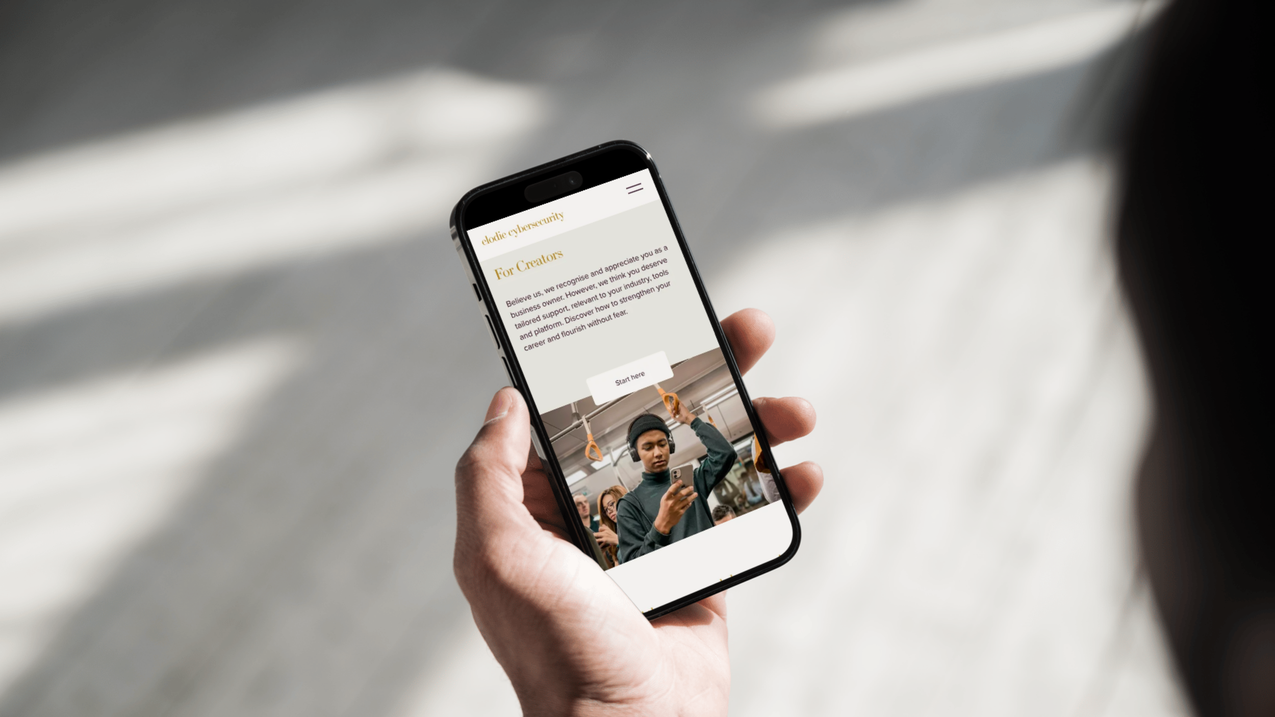 Person holding a smartphone displaying a webpage about cybersecurity for creators with a photo of a person in a hat and headphones on the screen, in a setting with a plain background.
