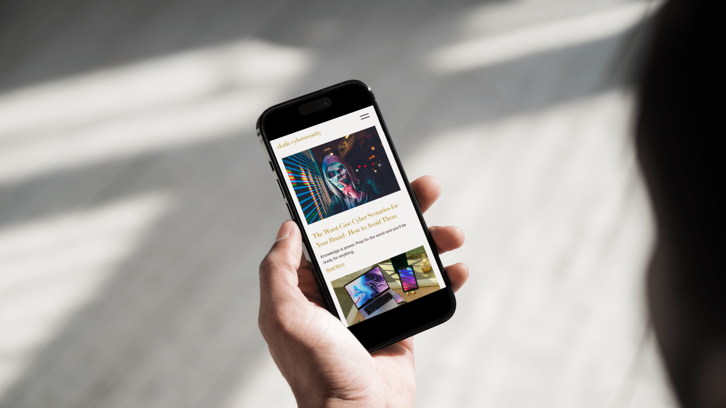Hand holding a smartphone displaying a website with cyber security content and images of electronic devices.