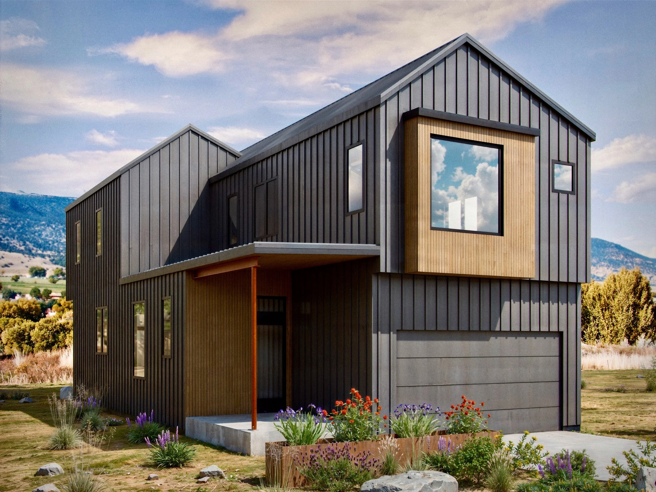 Modern two-story house with black vertical siding and large windows, surrounded by a landscaped yard with flowers and rocks, under a blue sky with clouds.