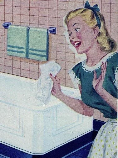 A woman smiling in a vintage style, standing in a bathroom with pink tiled walls, holding a white plastic bag on a counter, with a towel hanging on the wall behind her.
