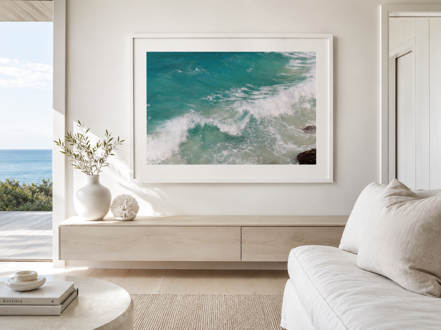 Living room with a large ocean wall art, white walls, a white sofa, a wooden console table, and a view of the beach outside.