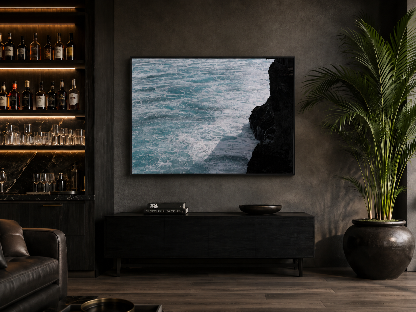Modern living room with a large wall-mounted TV showing ocean waves and cliffs, a black cabinet beneath with books and a black bowl, a tall green plant in a dark pot, and a bar area with bottles and glassware on lit shelves.