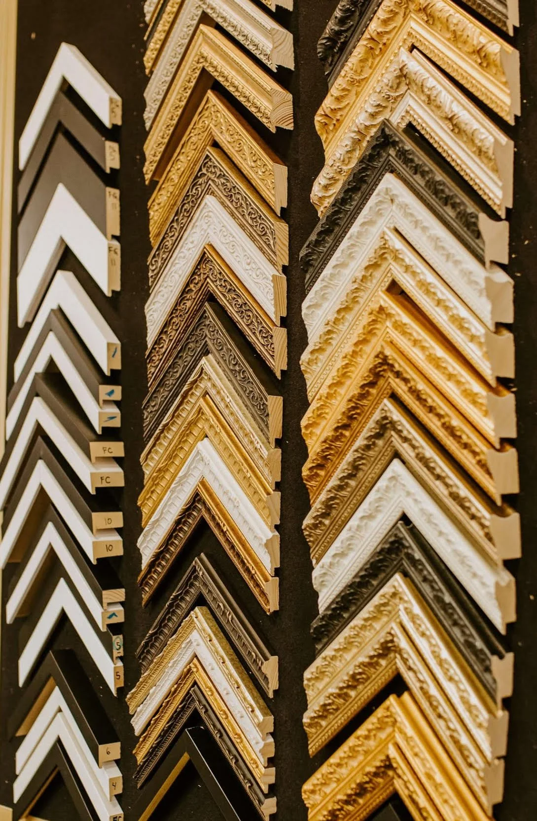 Display of various ornate picture frame corner samples in different colors and styles, arranged in rows.