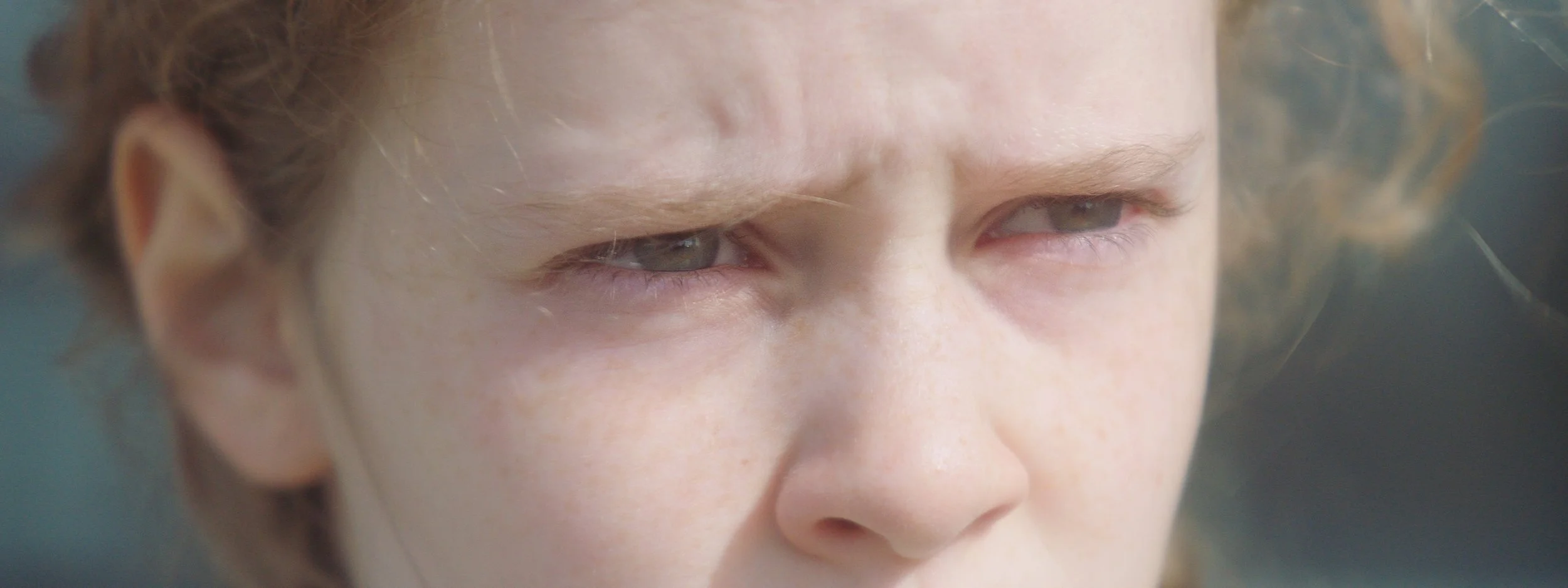Close-up of a person's face with curly hair, focusing on their eyes and forehead.