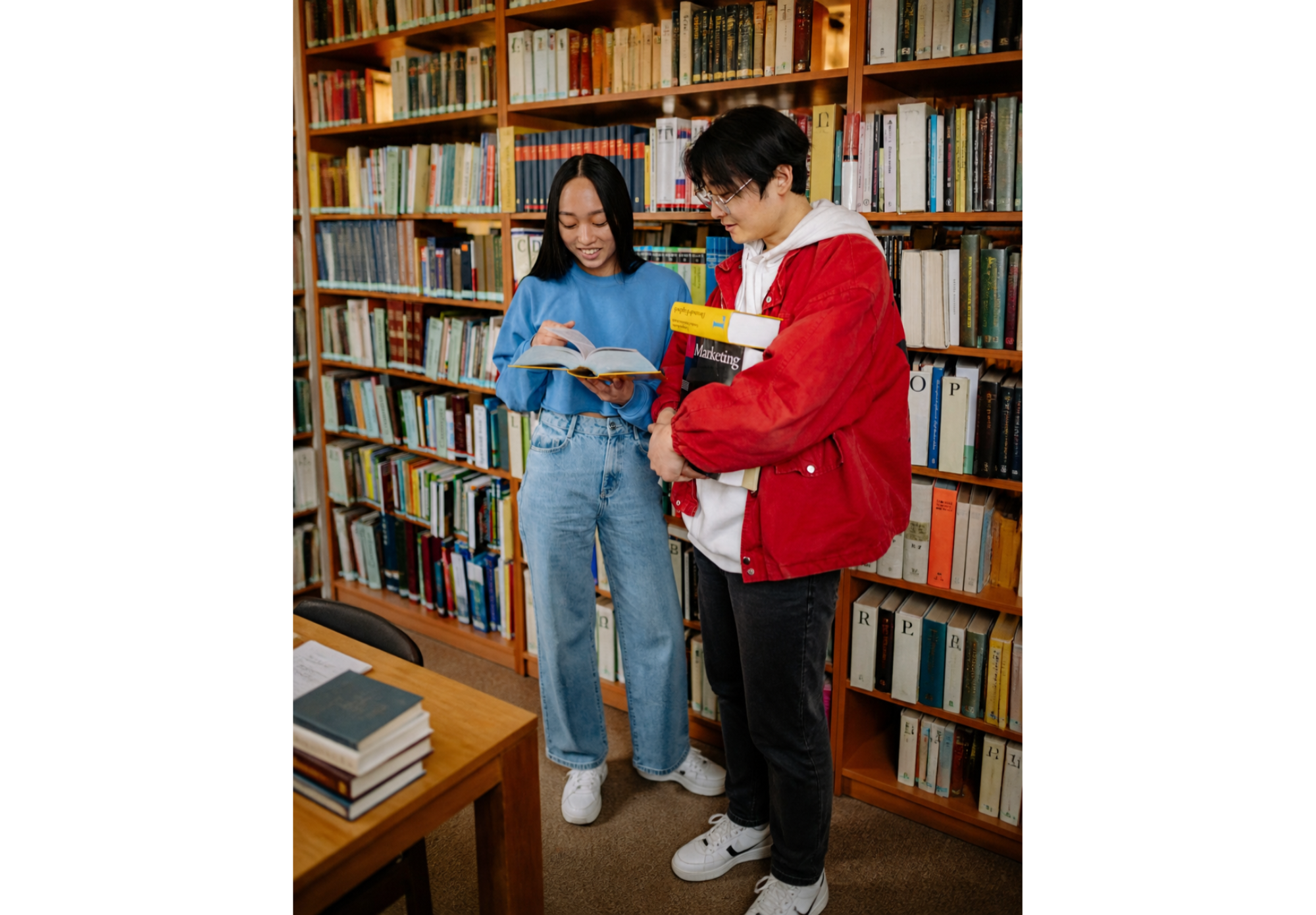 Two Korean and Chinese international student studying abroad in the U.S. America standing in a library and looking at a book for college