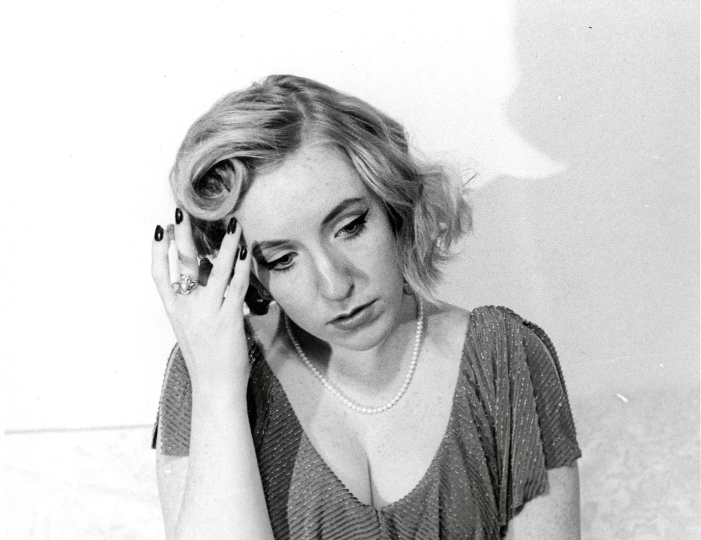 Black and white portrait of a woman with curly hair, wearing a pearl necklace, seated against a plain background.