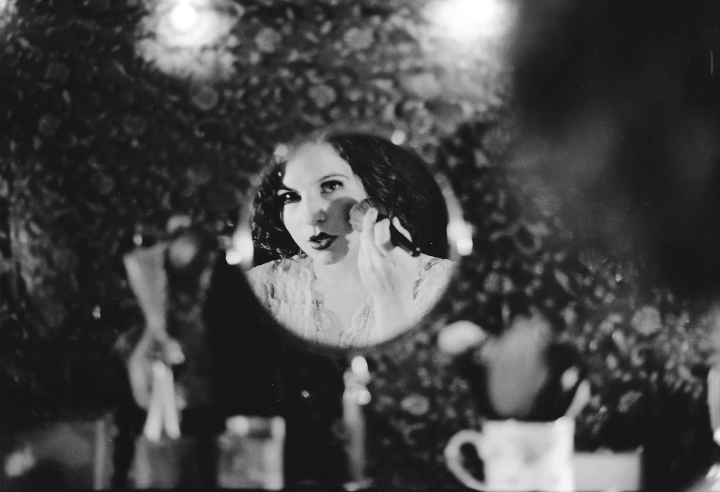 A woman looking into a mirror framed with small lights, applying makeup.