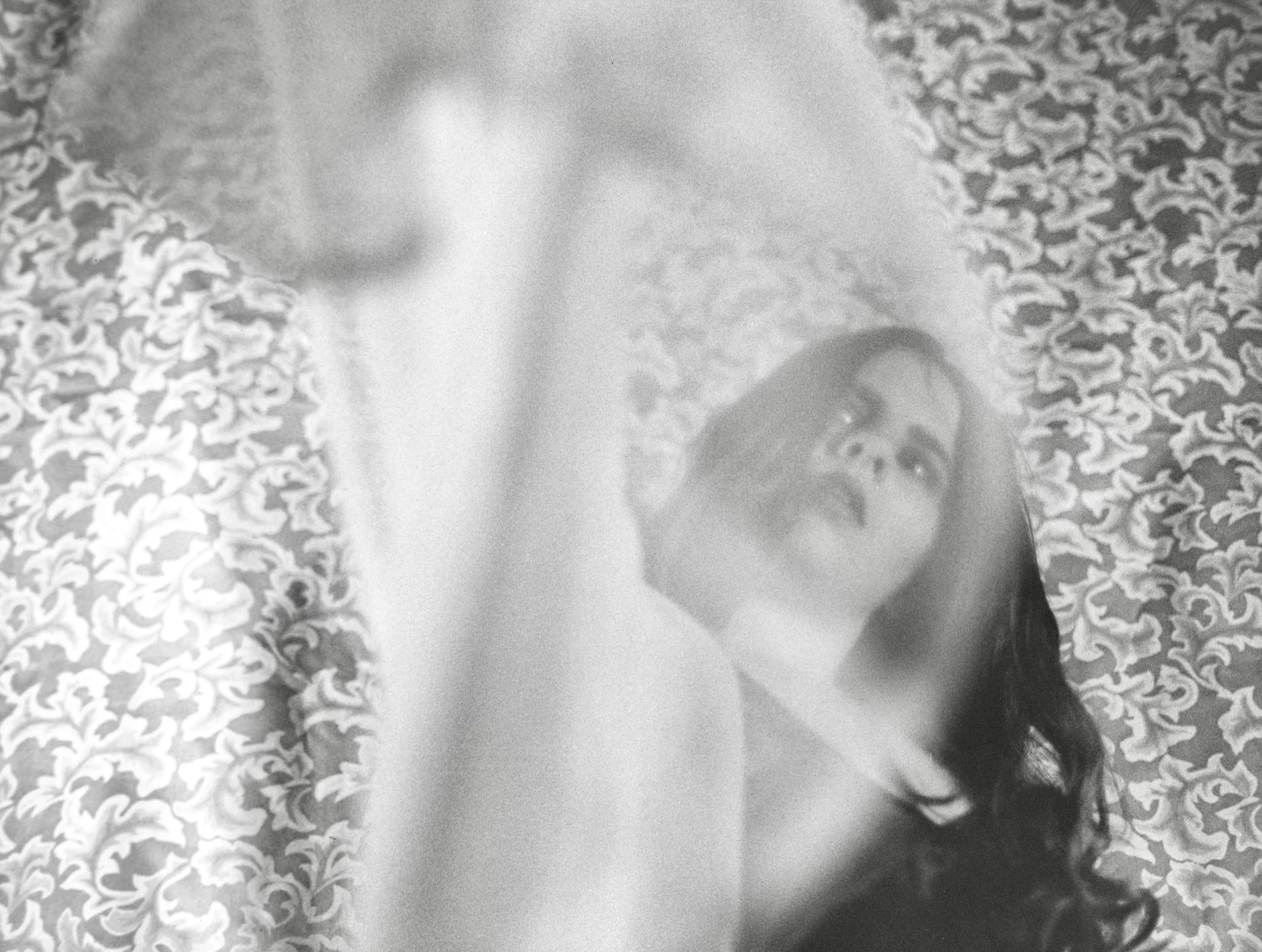 Black and white photo of a person with long dark hair, muddled almost entirely with shadows and blurred details, sitting on leopard print fabric, often found on clothing or upholstery.
