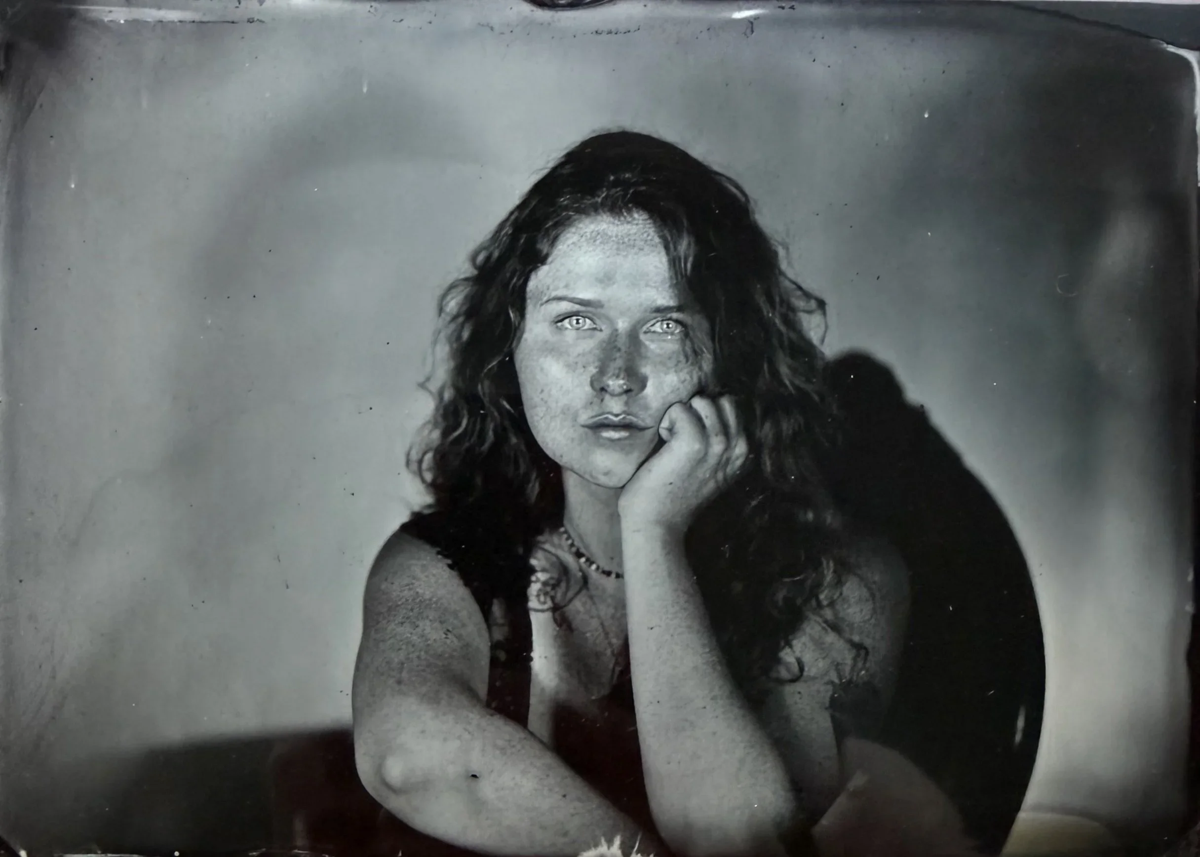 Black and white photo of a woman with curly hair, resting her chin on her hand, looking at the camera.