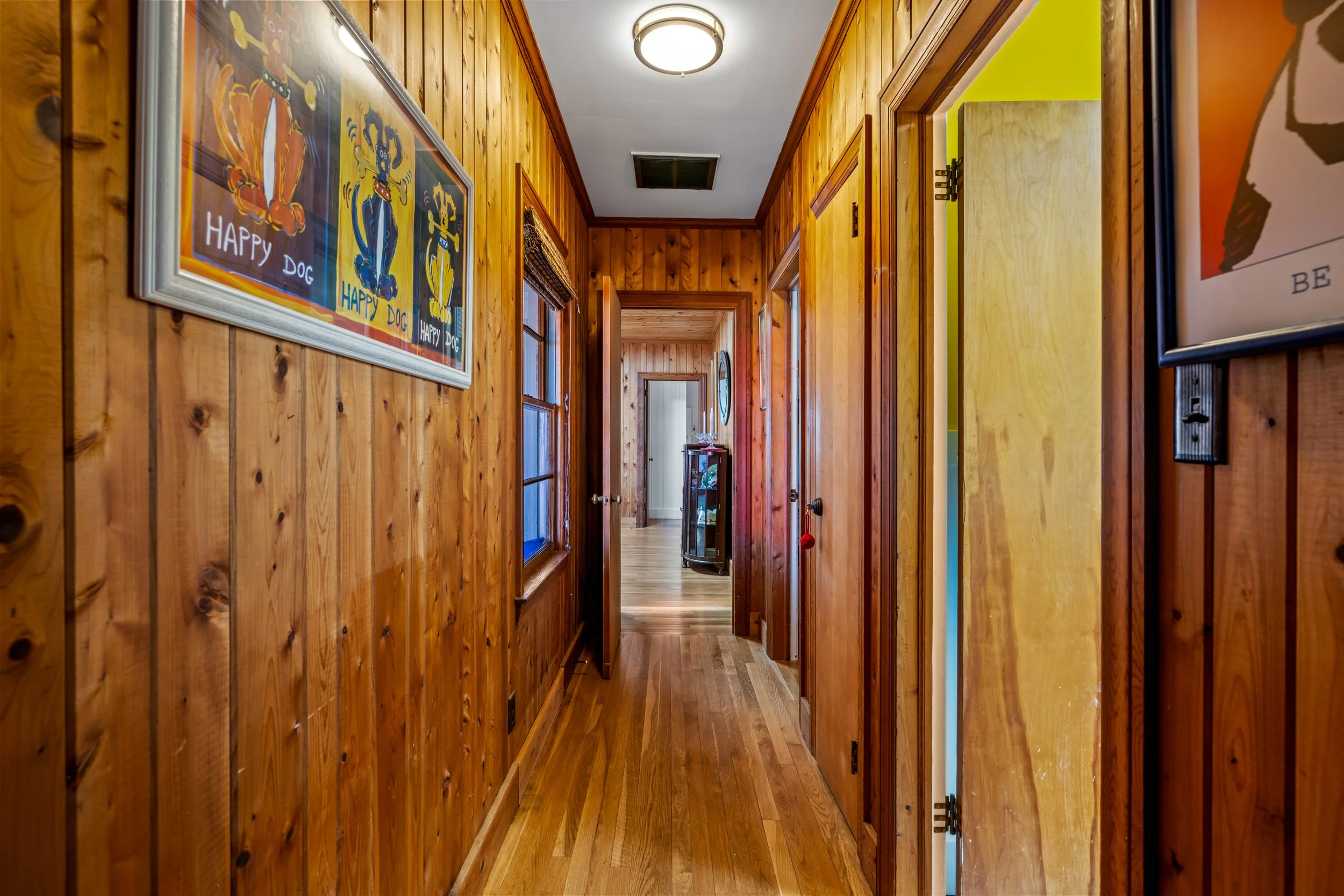 Wood-paneled hallway with art posters on the walls, a ceiling light fixture, and a wooden floor.