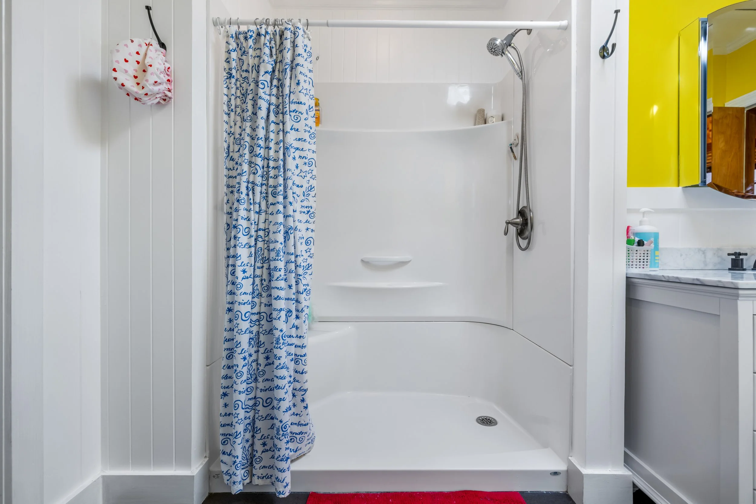 Bathroom with walk-in shower featuring a blue and white patterned shower curtain, a yellow cabinet with a mirror, and a white sink with toiletries on the counter.