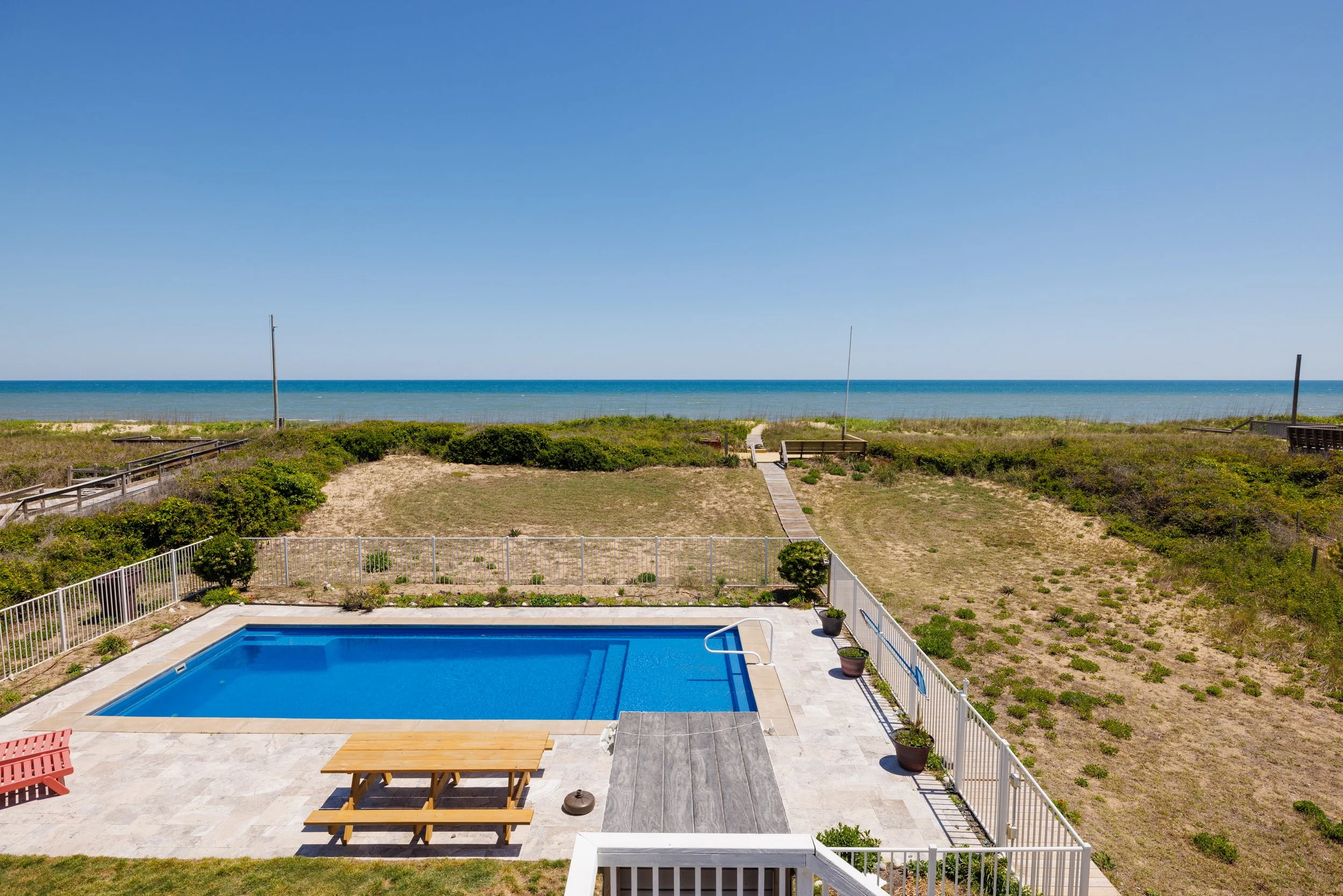 A backyard with a swimming pool, outdoor furniture, and a view of the ocean in the background.
