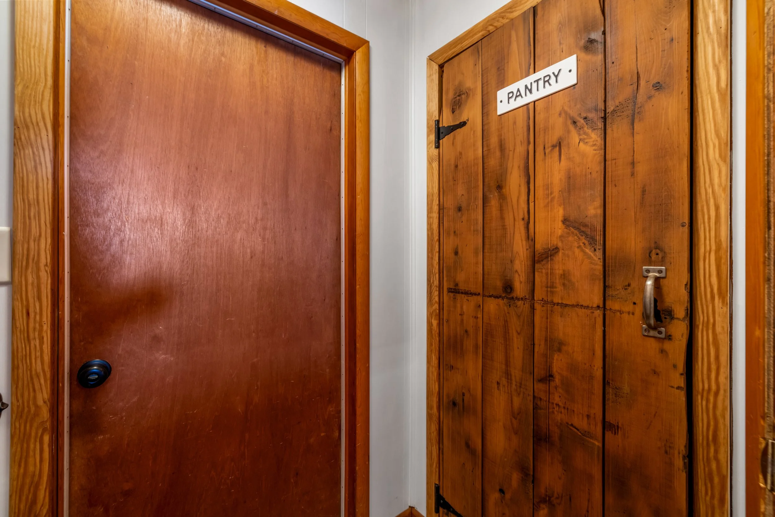 Wooden pantry door with a white sign that reads 'PANTRY' and a black handle, next to a plain brown door.