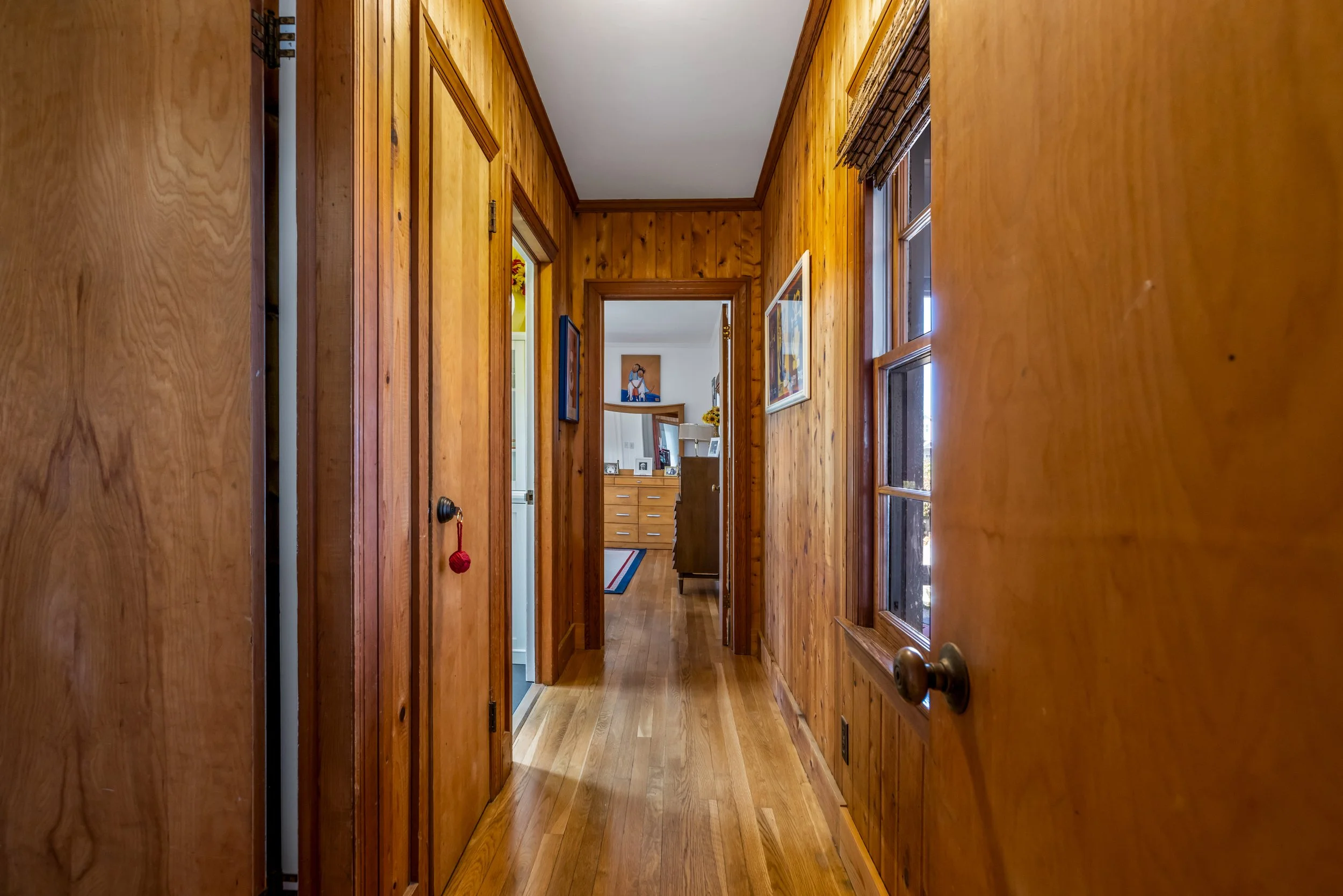 Wood-paneled hallway with hardwood floors, leading to a room with furniture and wall art visible in the distance.
