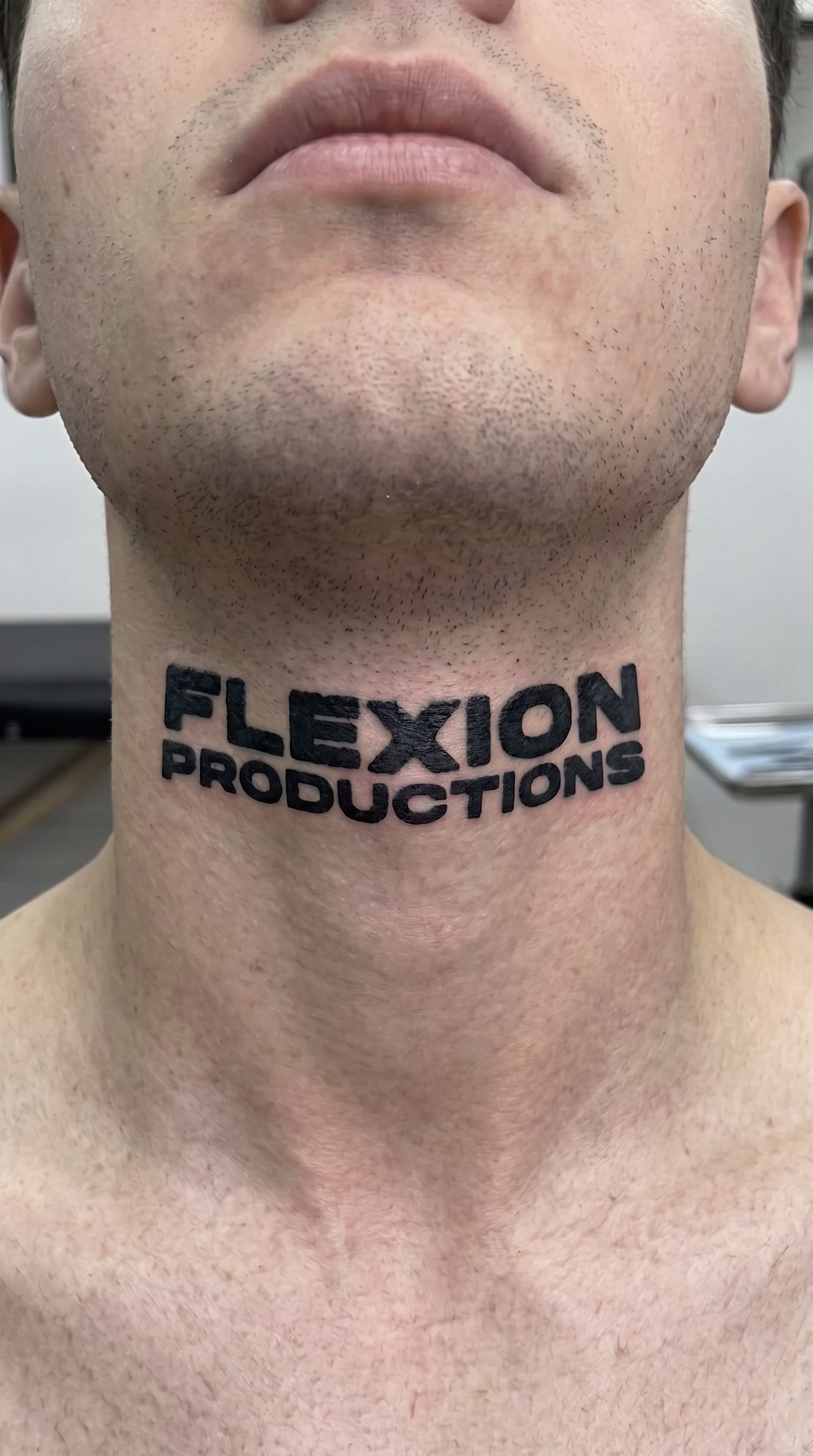 Close-up of a person's neck with a tattoo that reads 'FLEXION PRODUCTIONS' in bold black letters.