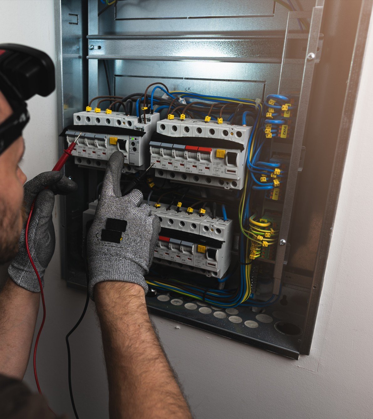 Un électricien travaillant sur un tableau électrique, utilisant un multimètre pour tester les connexions.