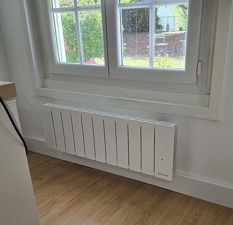 Un radiateur connecté Intuis Beladoo Nativ modèle plinthe installé sous une fenêtre dans un bureau