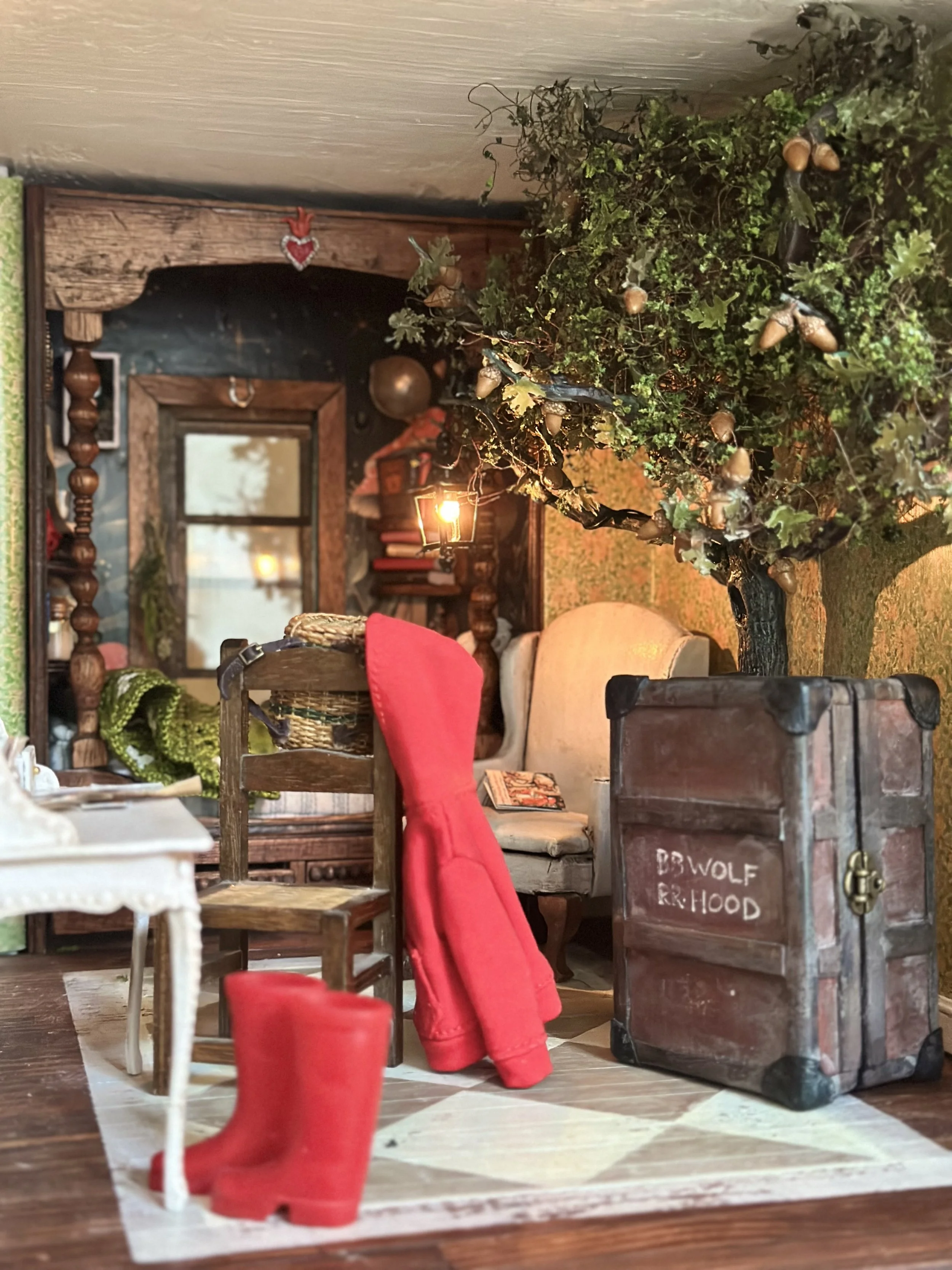 Decorative indoor scene with a small white table, a wooden chair with a red hoodie, a vintage-style upright trunk, a plush chair with a book, a large oak tree with acorns, bed nook, and a warm light from a lantern.