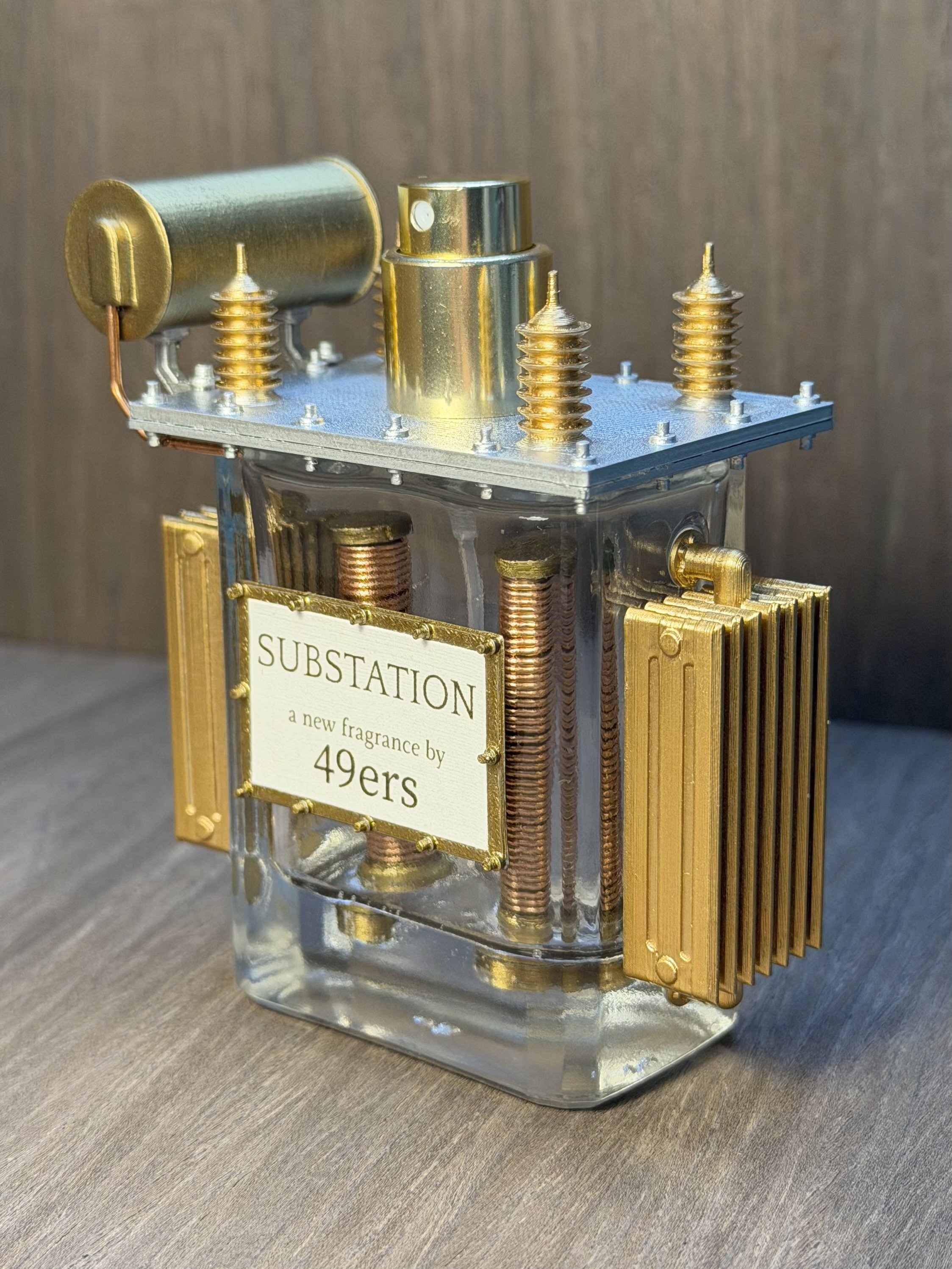 Close-up of a decorative perfume bottle with a transparent glass base, gold-colored metal accents, and a label reading 'Substation' on the front.
