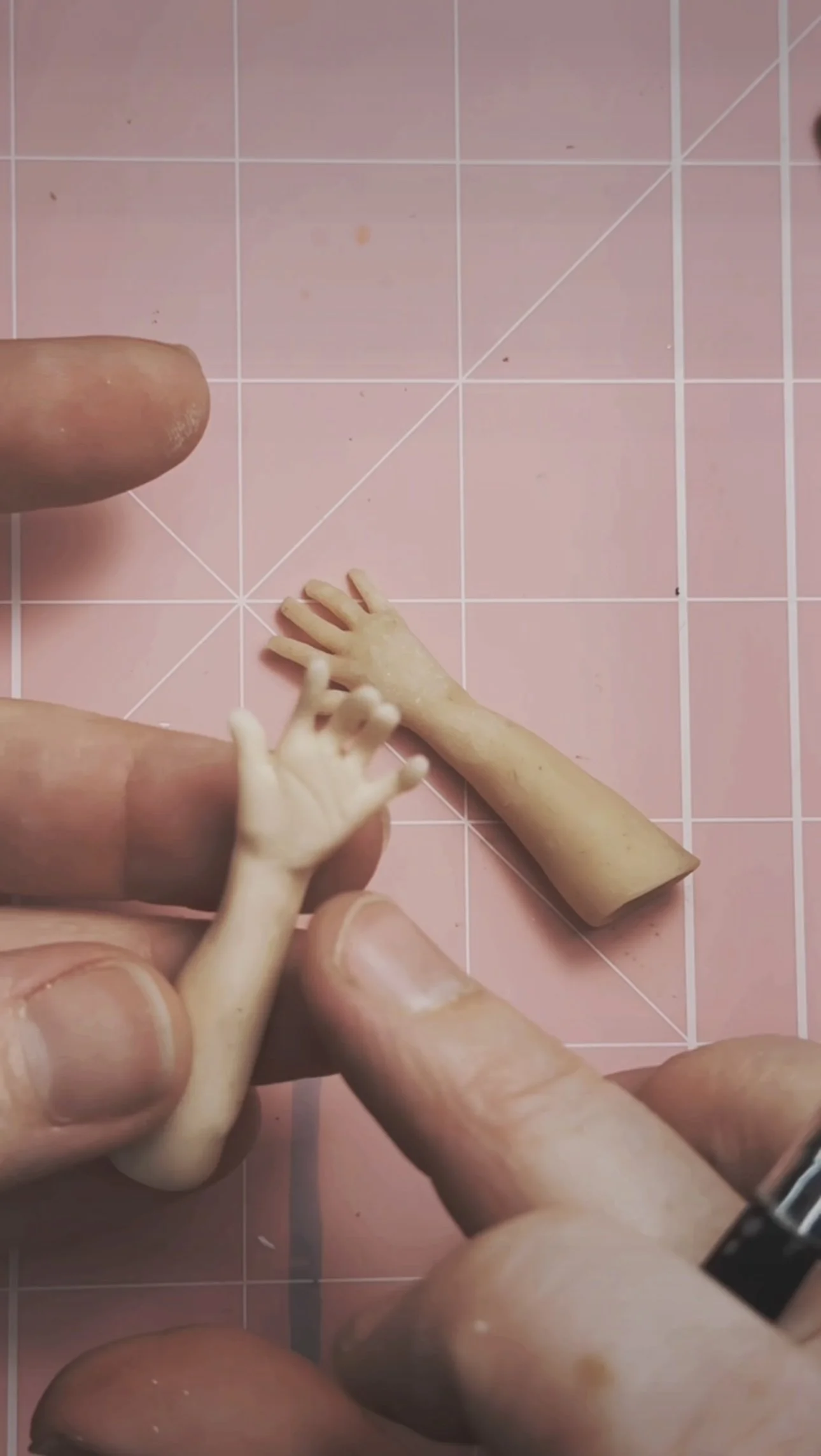 Close-up of a person holding a small sculpted doll's hand against a pink mat.