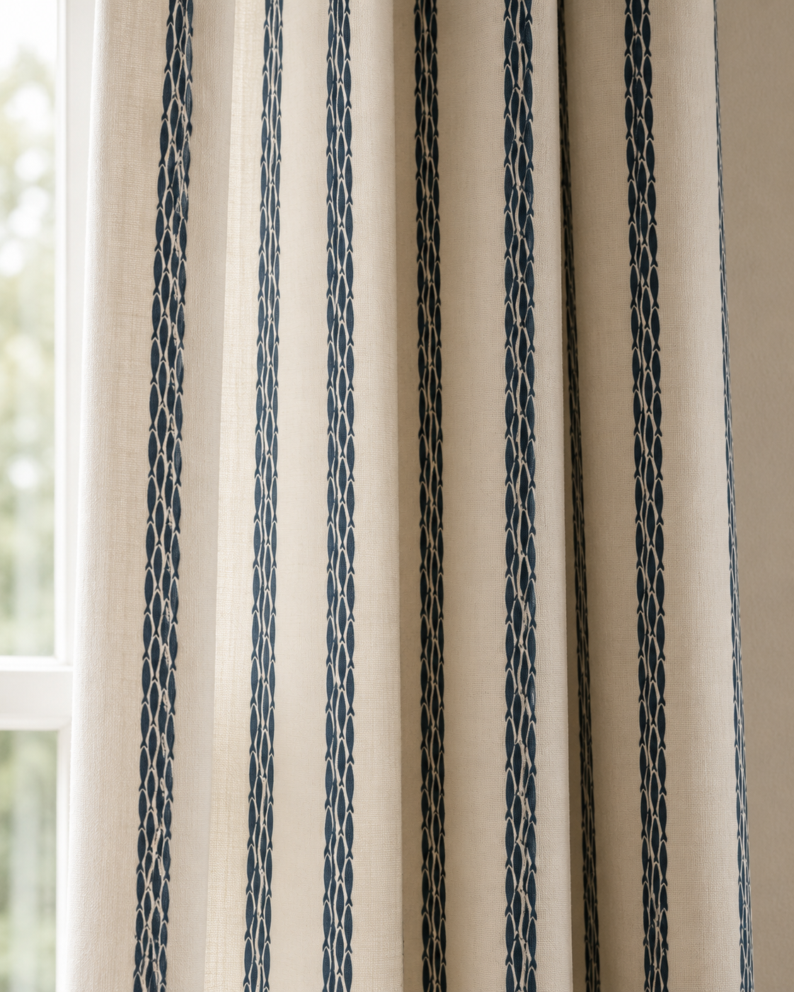 Close-up of beige curtains with blue vertical stripe pattern hanging in front of a window with a view of trees outside.