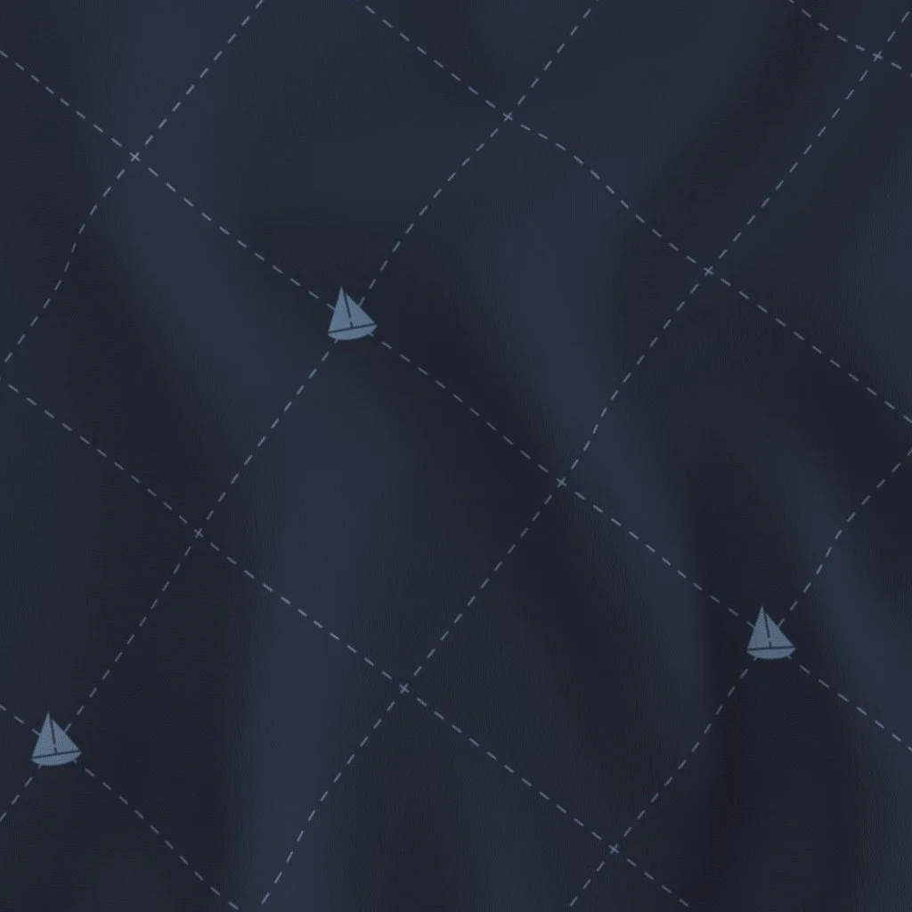 Close-up of navy blue fabric with a nautical pattern of small sailing boats and dashed lines forming a grid.