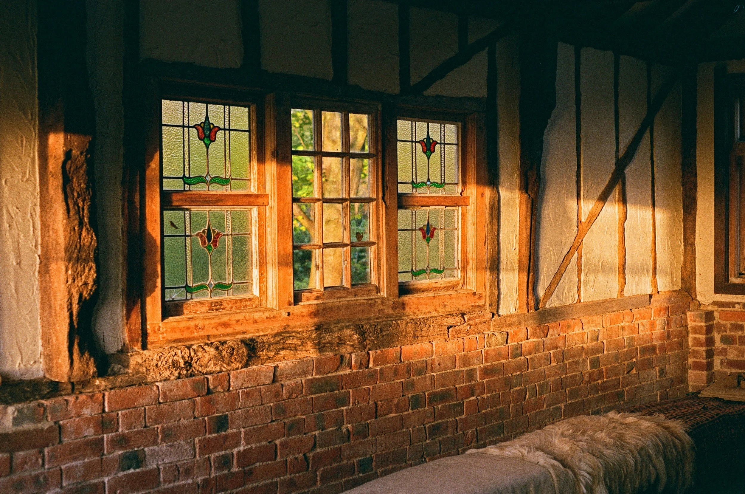 interior of old cottage with traditional lath and plaster finish. sunlight is coming through the stained glass windows