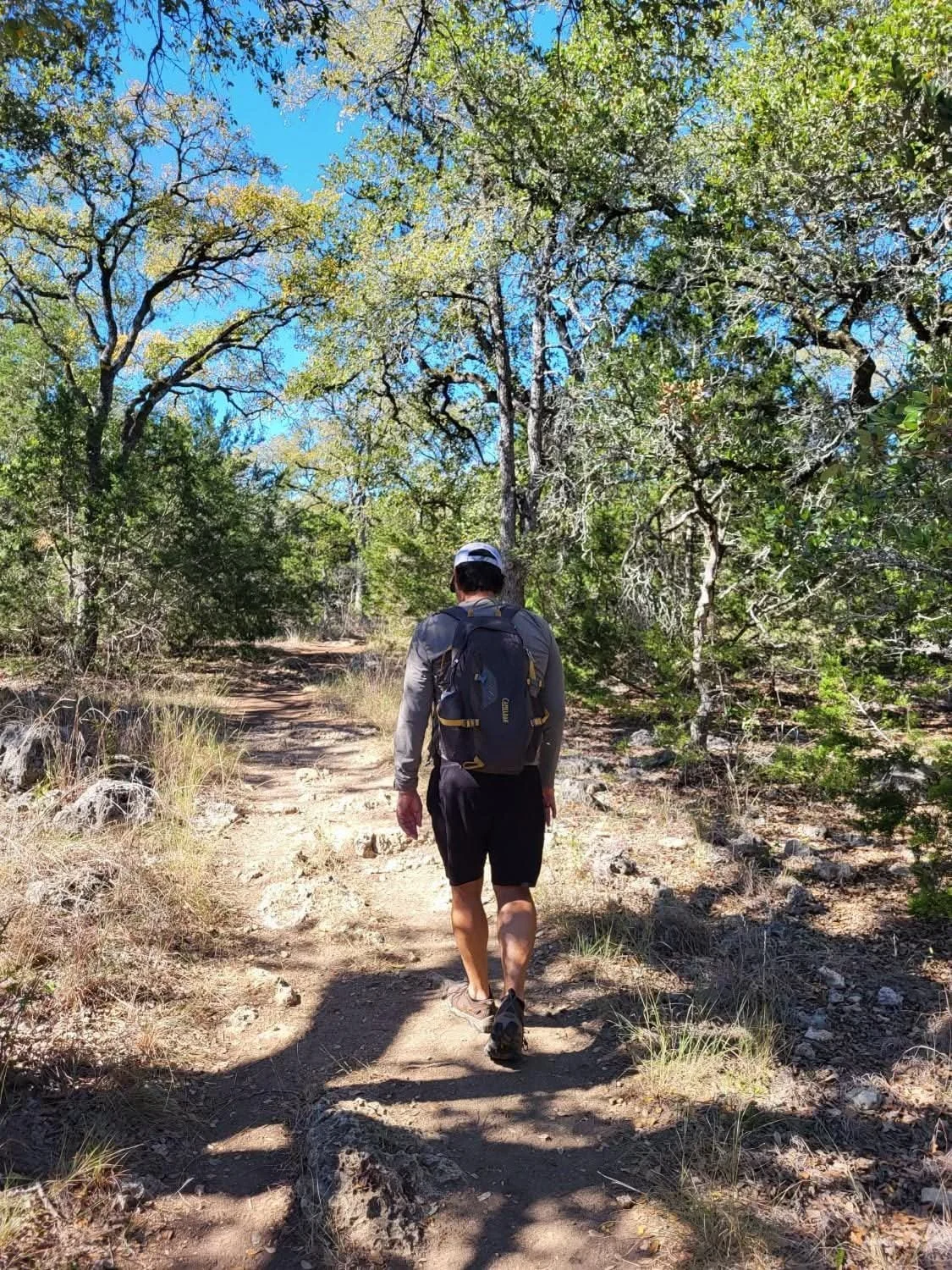 Steven Stinnett hiking in Colorado on a dirt trail through a forested area with green trees and blue sky overhead.