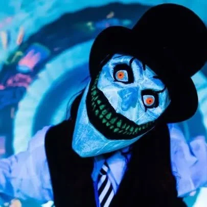 Distorted neon-faced nightmare character with glowing eyes and surreal costume design inside an immersive blacklight haunted attraction experience at ScareHouse.