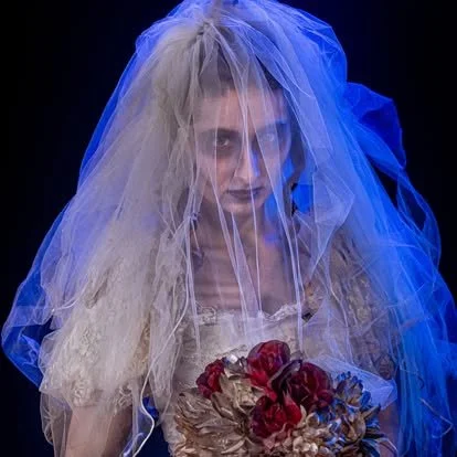 Haunted ghost bride in a tattered wedding gown holding wilted flowers beneath a veil, creating a dramatic supernatural scene inside a Pittsburgh haunted attraction.