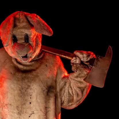 Terrifying creepy rabbit character wielding a large axe inside a professional haunted attraction, featuring immersive horror makeup, theatrical lighting, and live scare actors at ScareHouse.