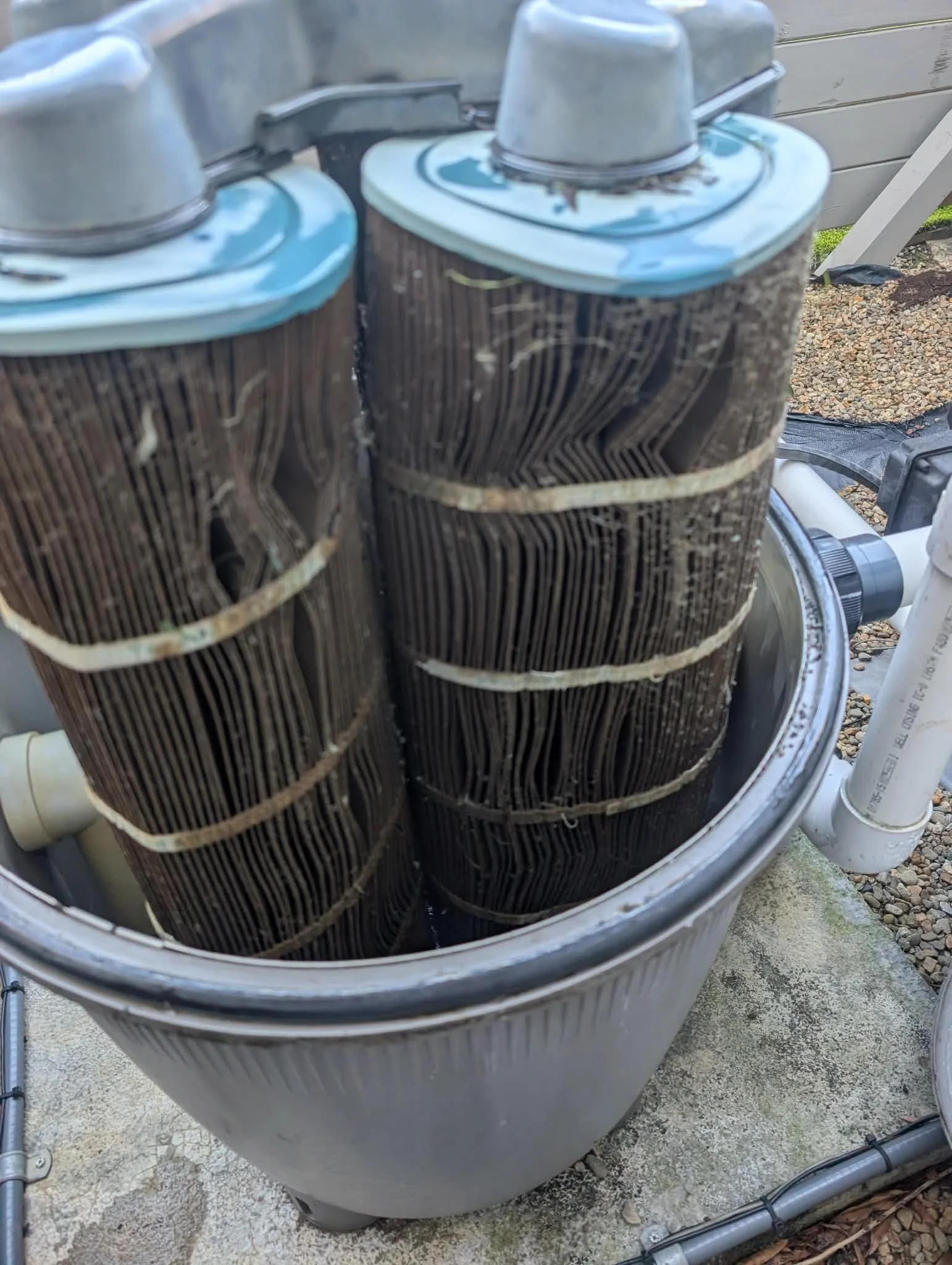 Close-up of an outdoor evaporative cooler's cooling pads inside a metal casing, with some water visible on the pads and around the base, and plumbing components nearby.