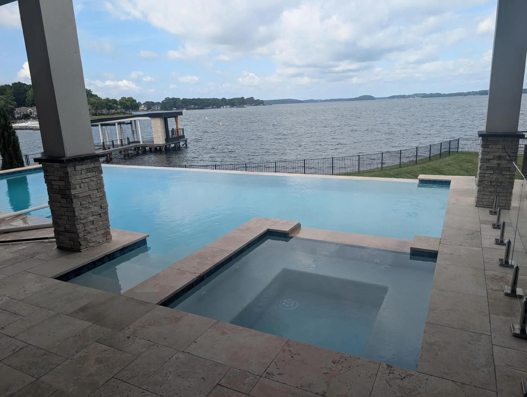 View from a covered patio looking out over a lake with houses along the shoreline, a boat, and a partly cloudy sky.