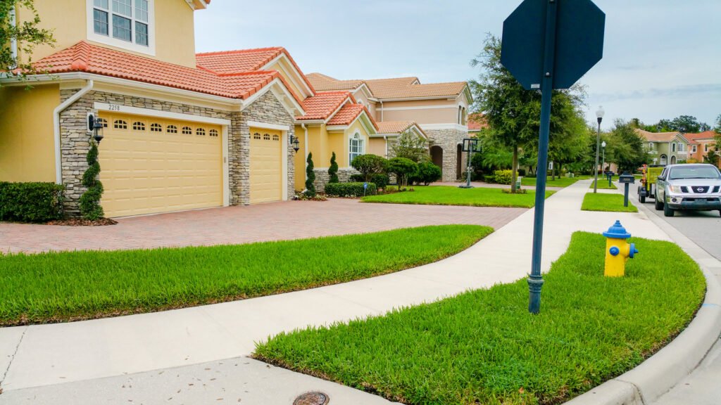 Residential neighborhood with yellow houses, well-kept lawns, driveways, street lamps, a stop sign, a fire hydrant, and parked cars.