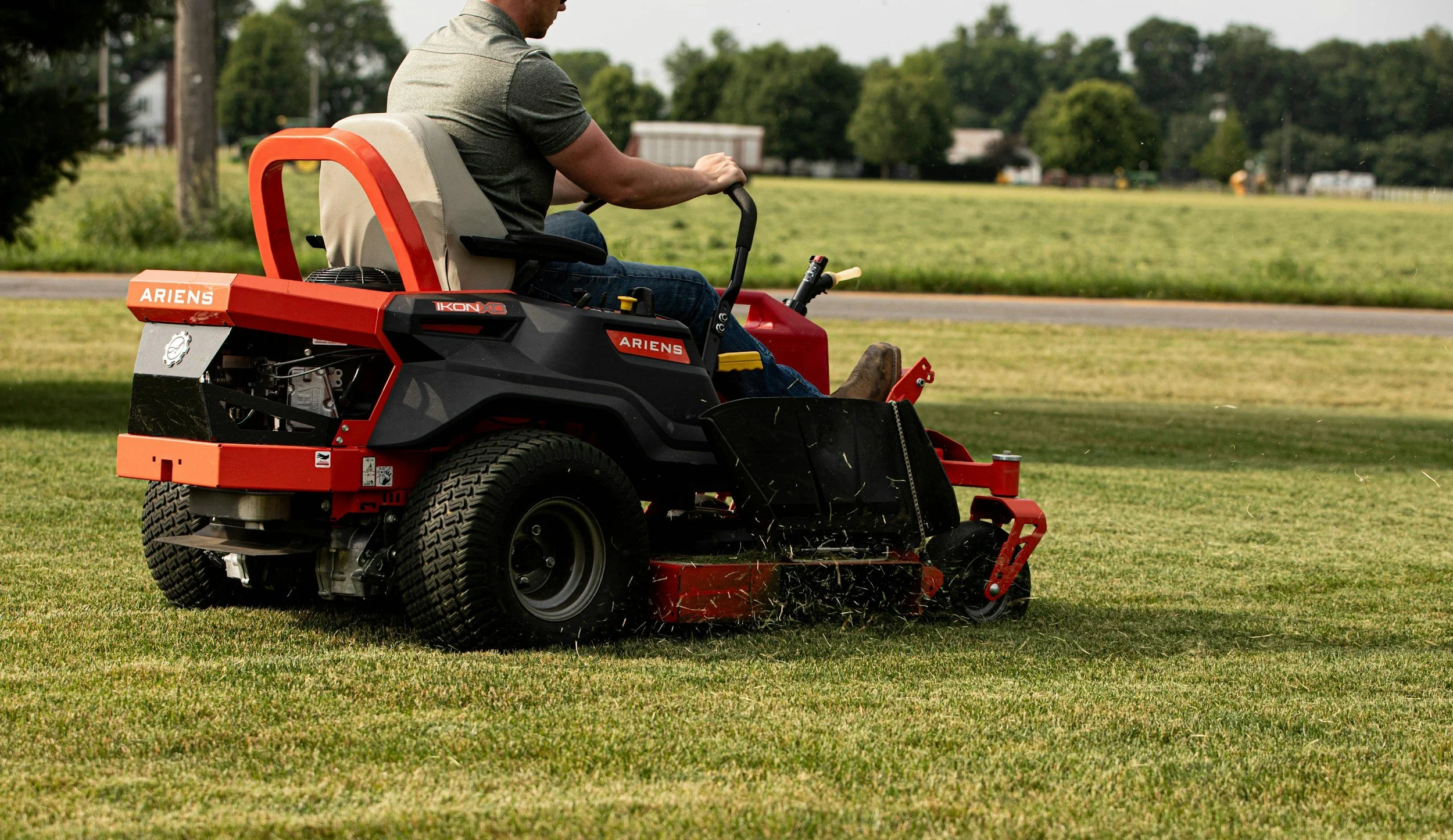 A man operating a red and black Ariens IKON XD lawn mower on a green grassy field outdoors.
