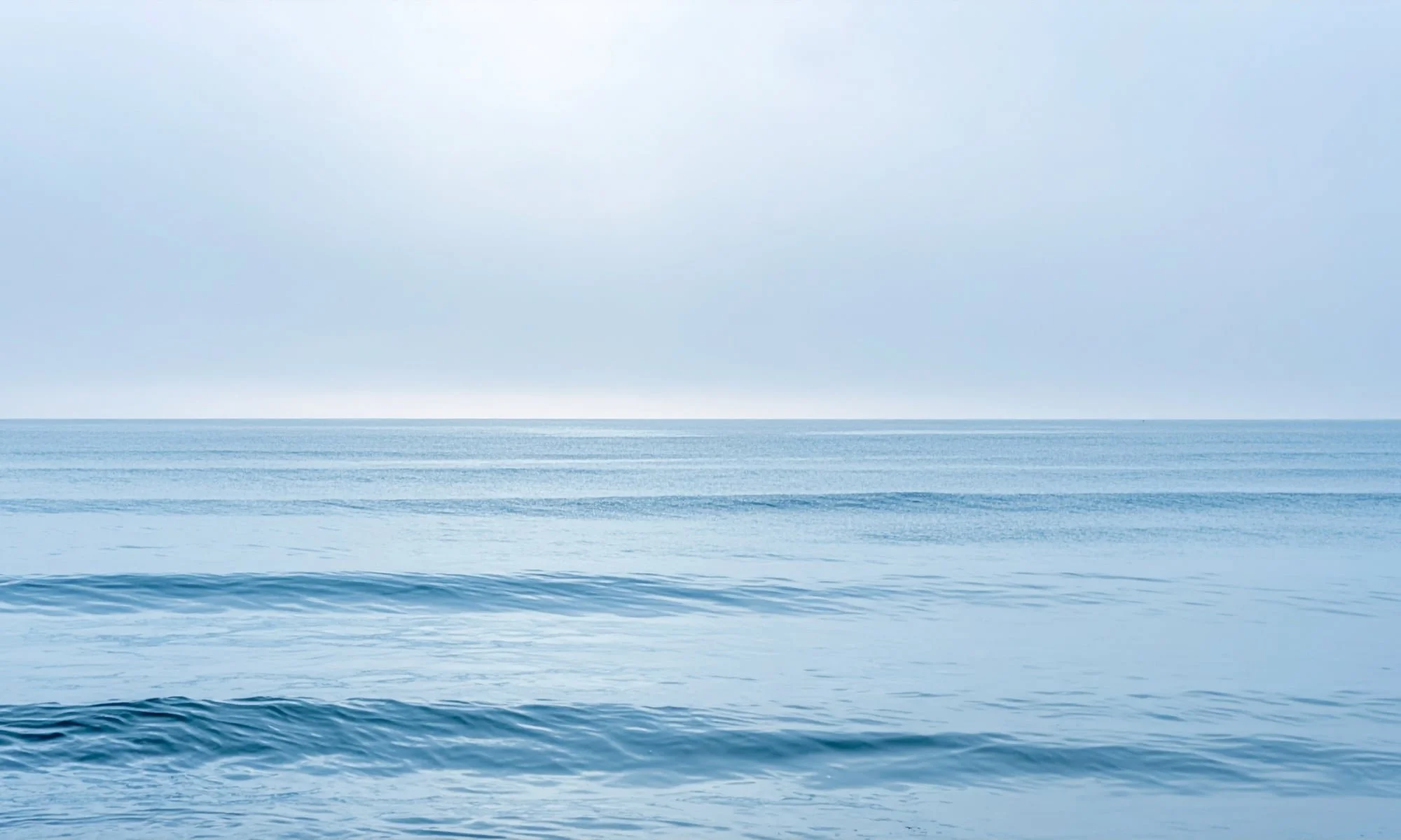 A vast ocean with gentle waves under a cloudy sky.