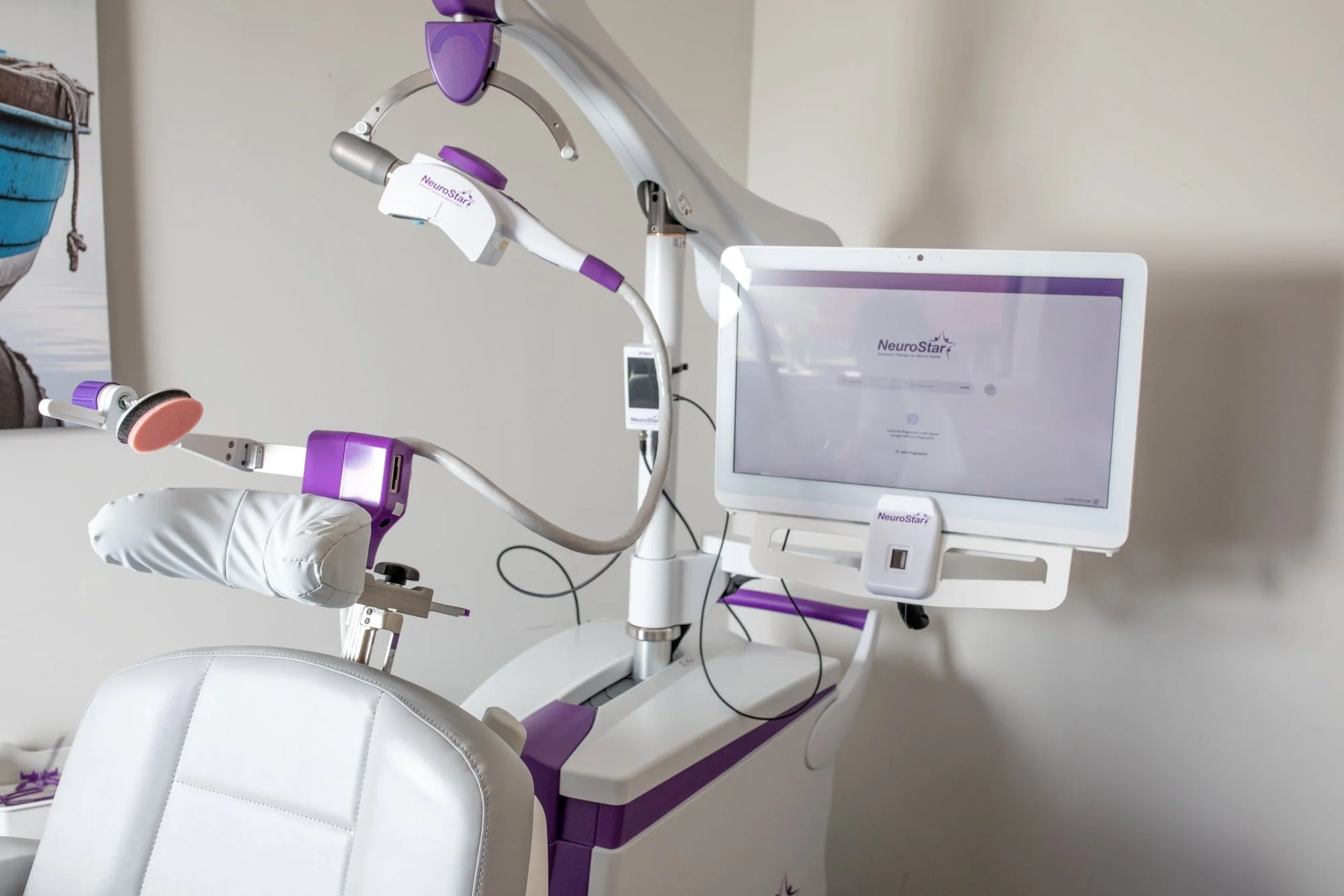 Medical chair attached to a NeuroStar transcranial magnetic stimulation (TMS) machine with a computer monitor displaying the NeuroStar logo.