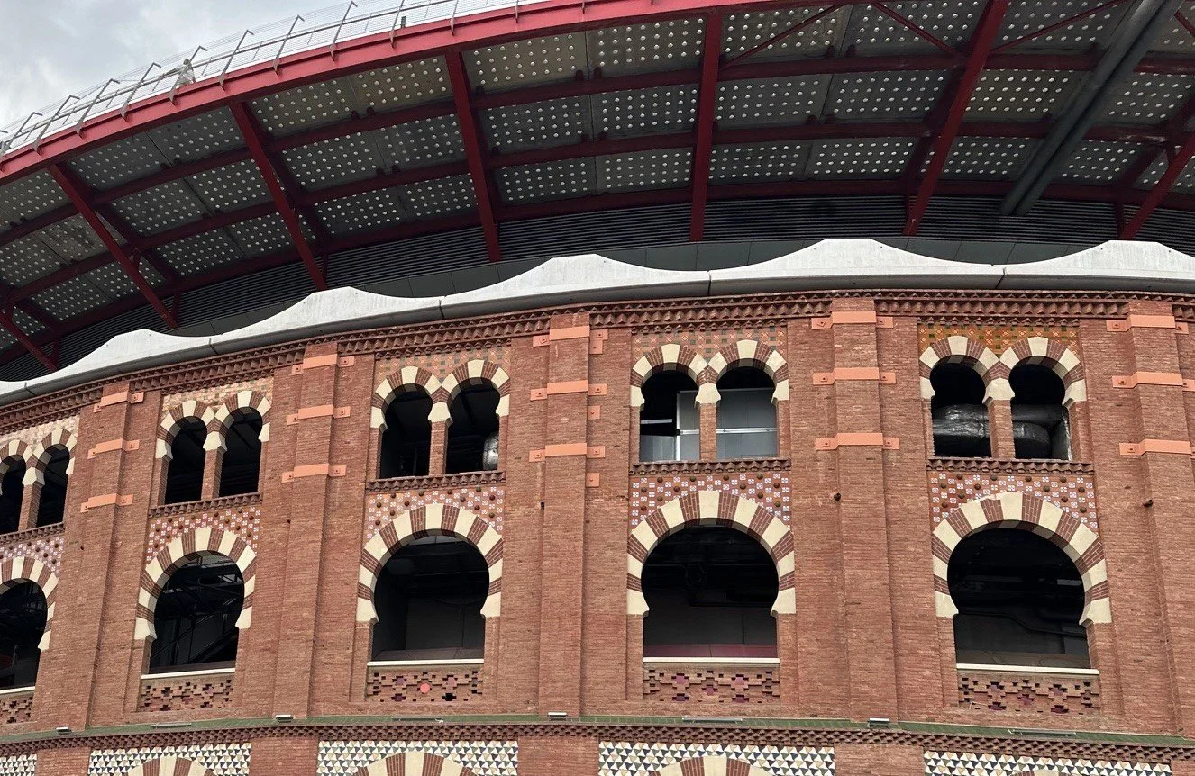 A portion of a brick sports stadium with arched windows and a modern roof structure above.