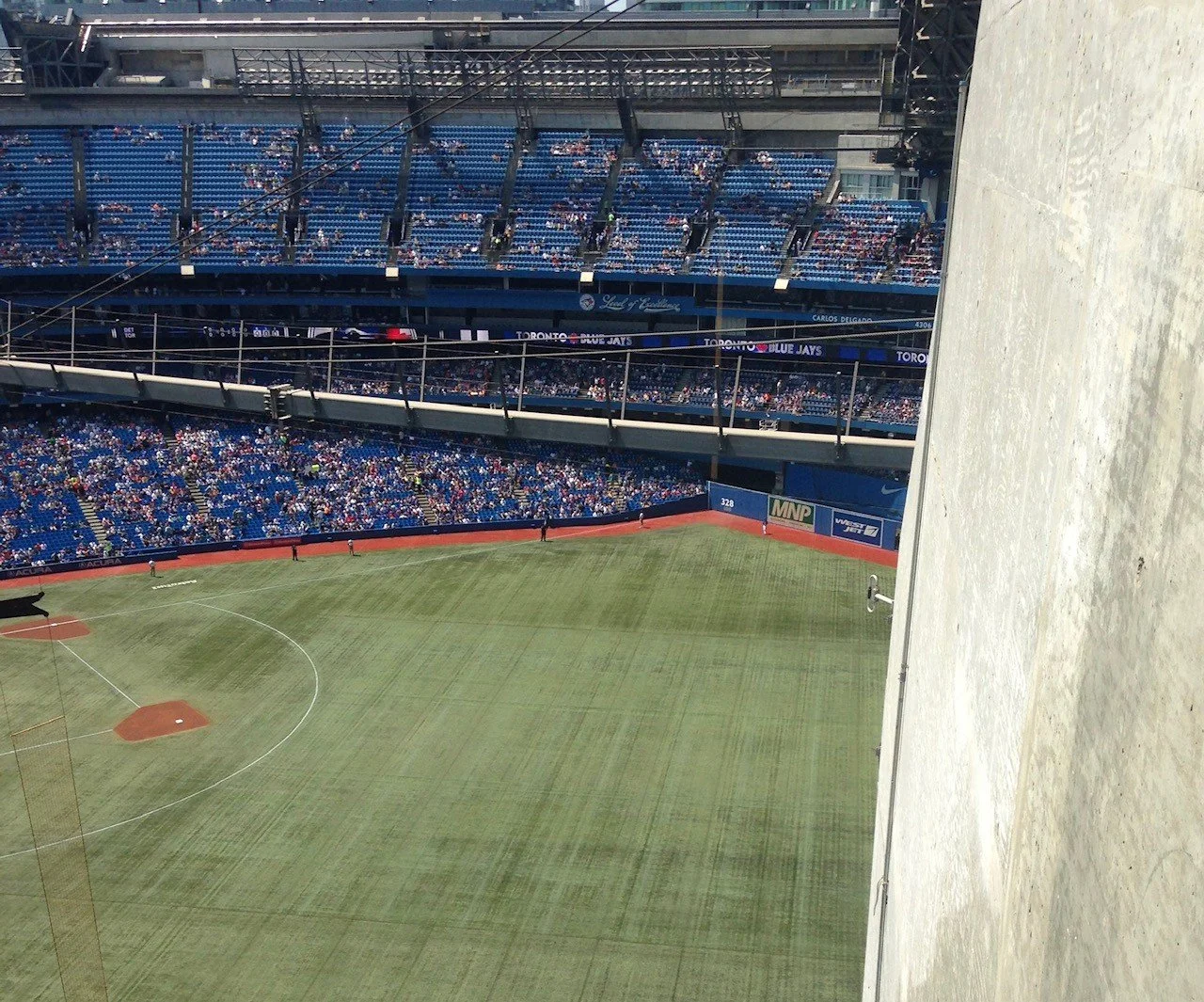 View of a baseball stadium with a field and spectators in the stands, seen from a high vantage point with a wall on the right side.