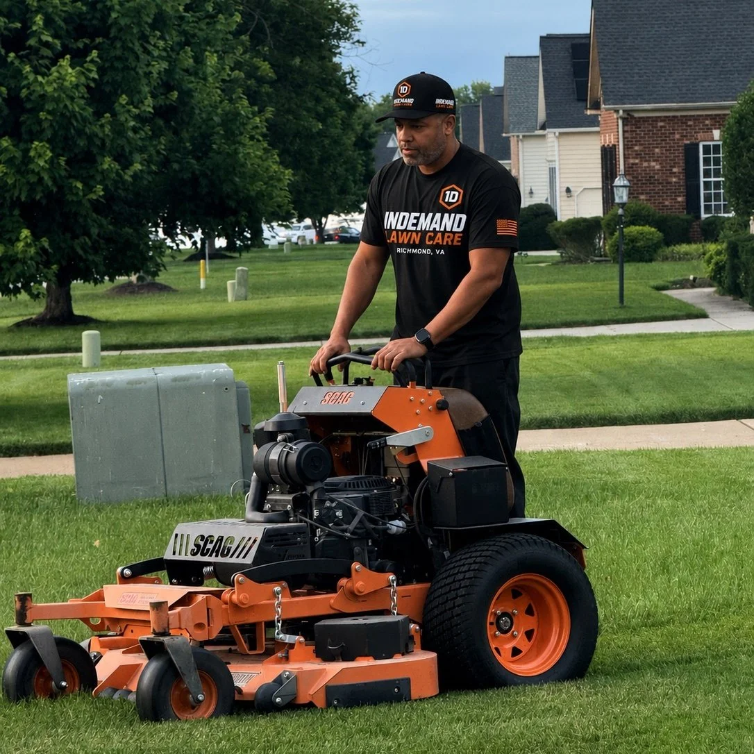 A man operating a zero-turn lawn mower on a lush green lawn in a suburban neighborhood.