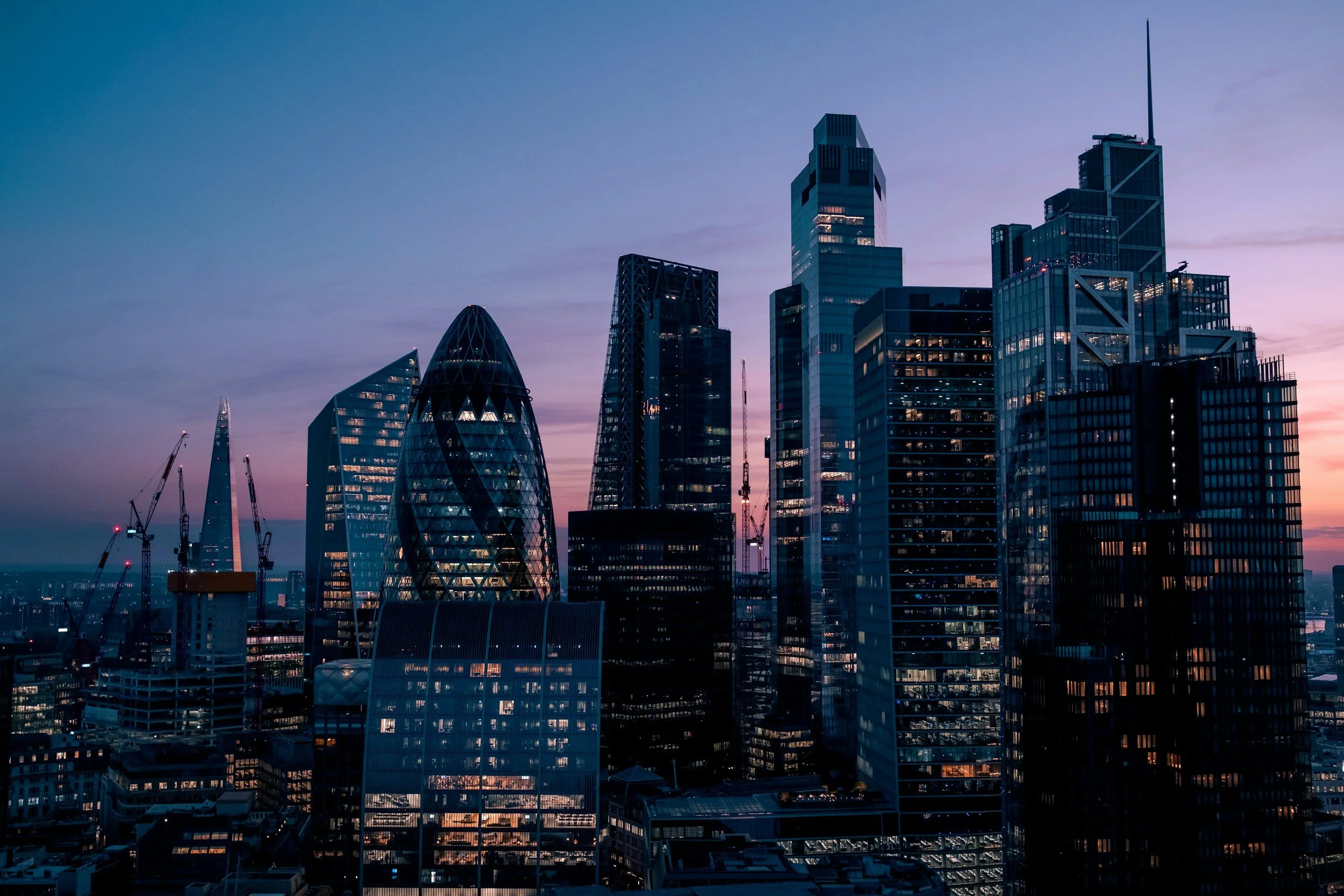 City skyline with modern glass skyscrapers at dusk, under a purple and pink sky.