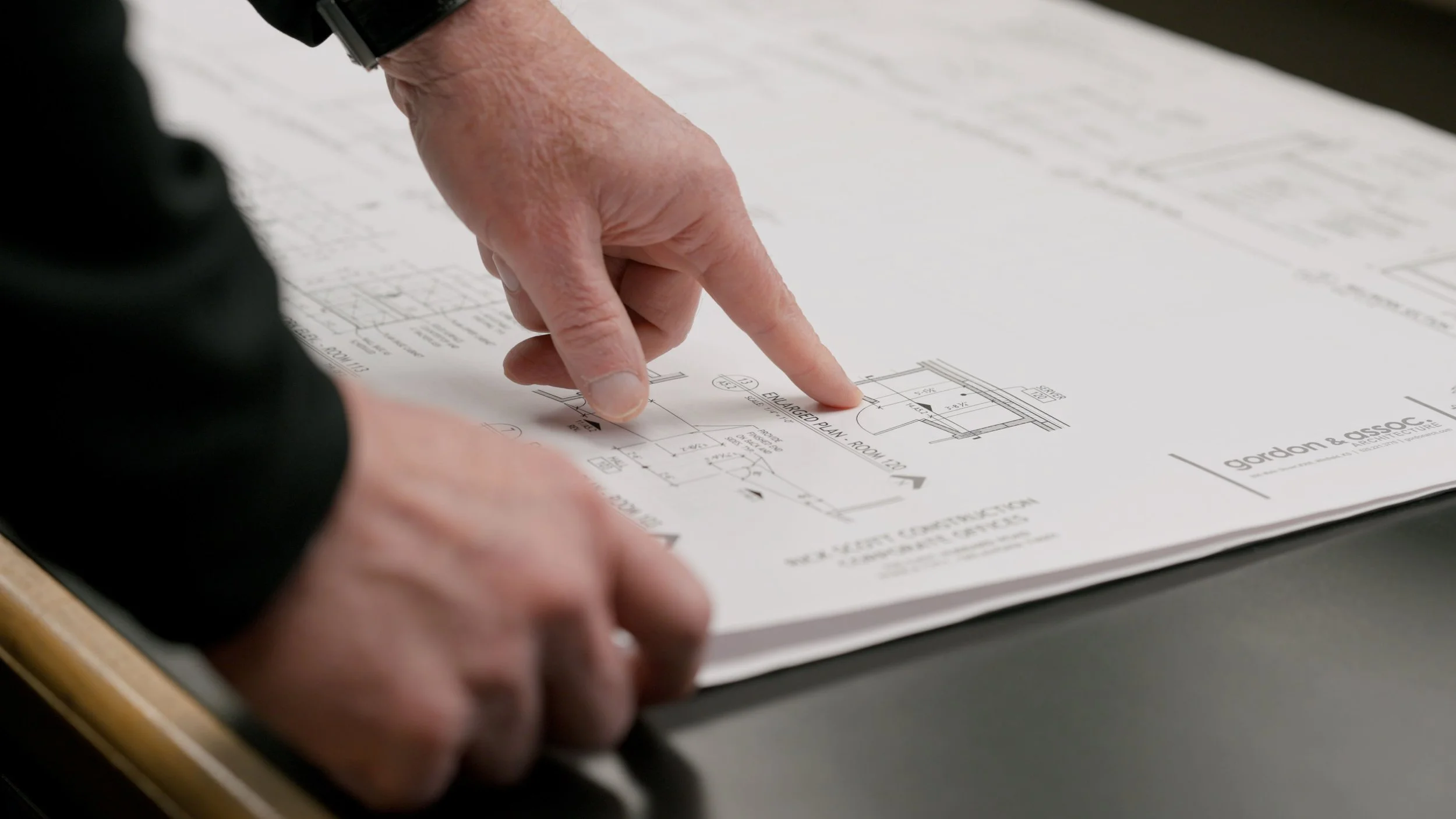 Close-up of a hand pointing at an architectural blueprint on a table.
