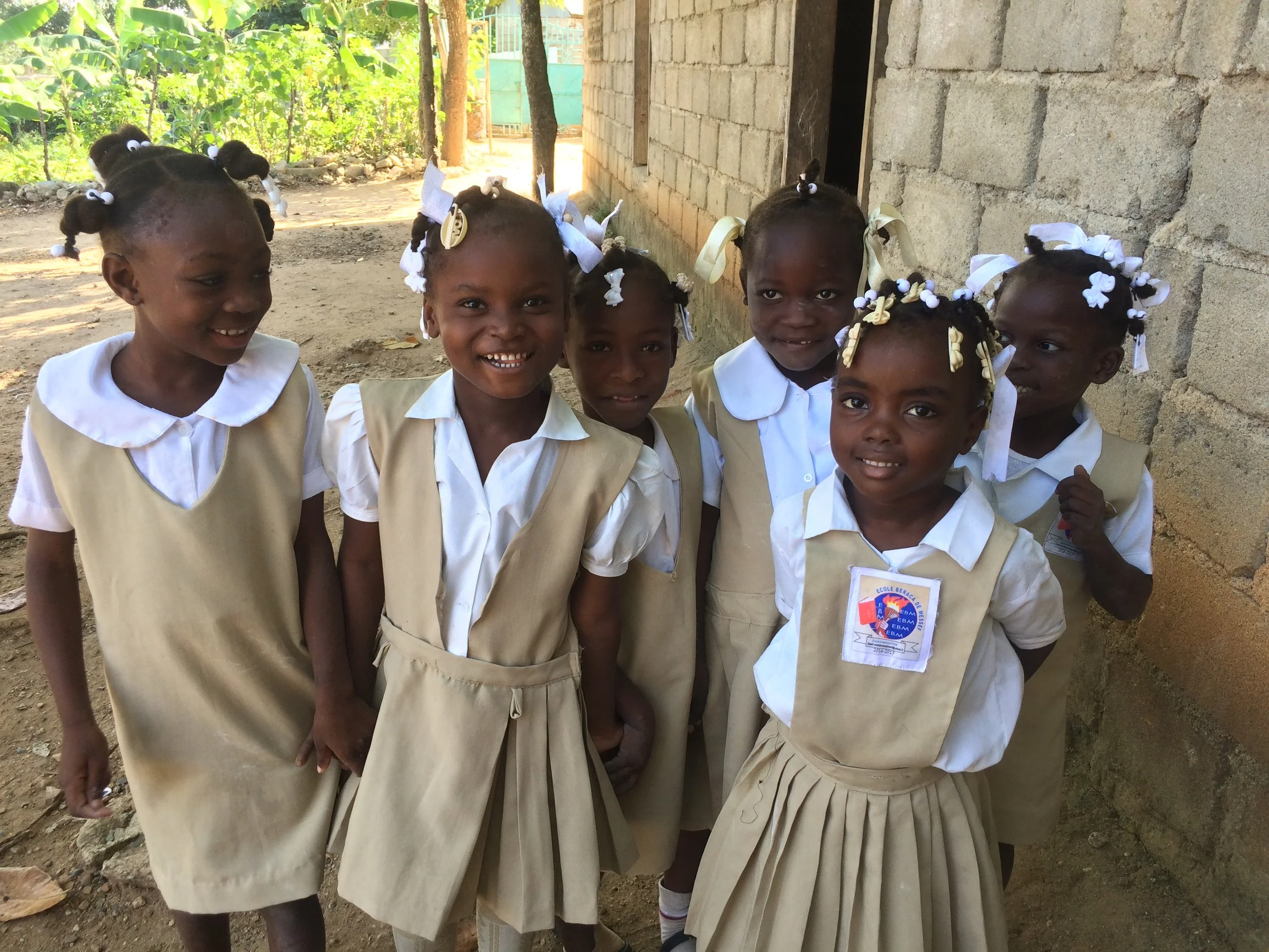 A group of young African girls in school uniforms standing outside next to a building, smiling for the camera.