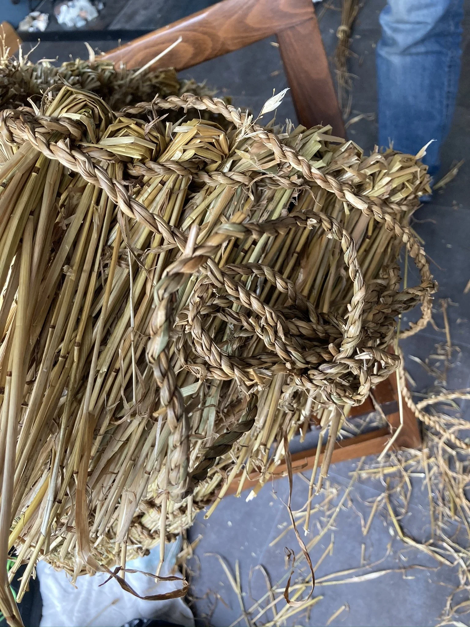 A close-up view of woven straw and grass ropes, some with decorative braiding, on a wooden and metal surface.